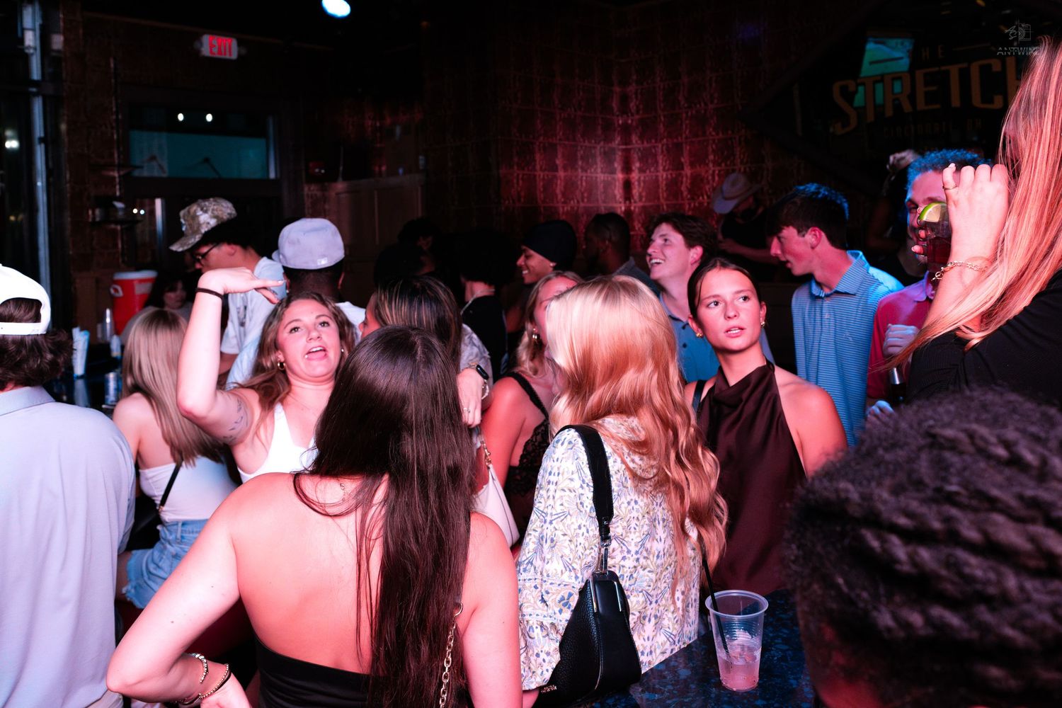Crowd of young people socializing at a busy indoor bar venue.