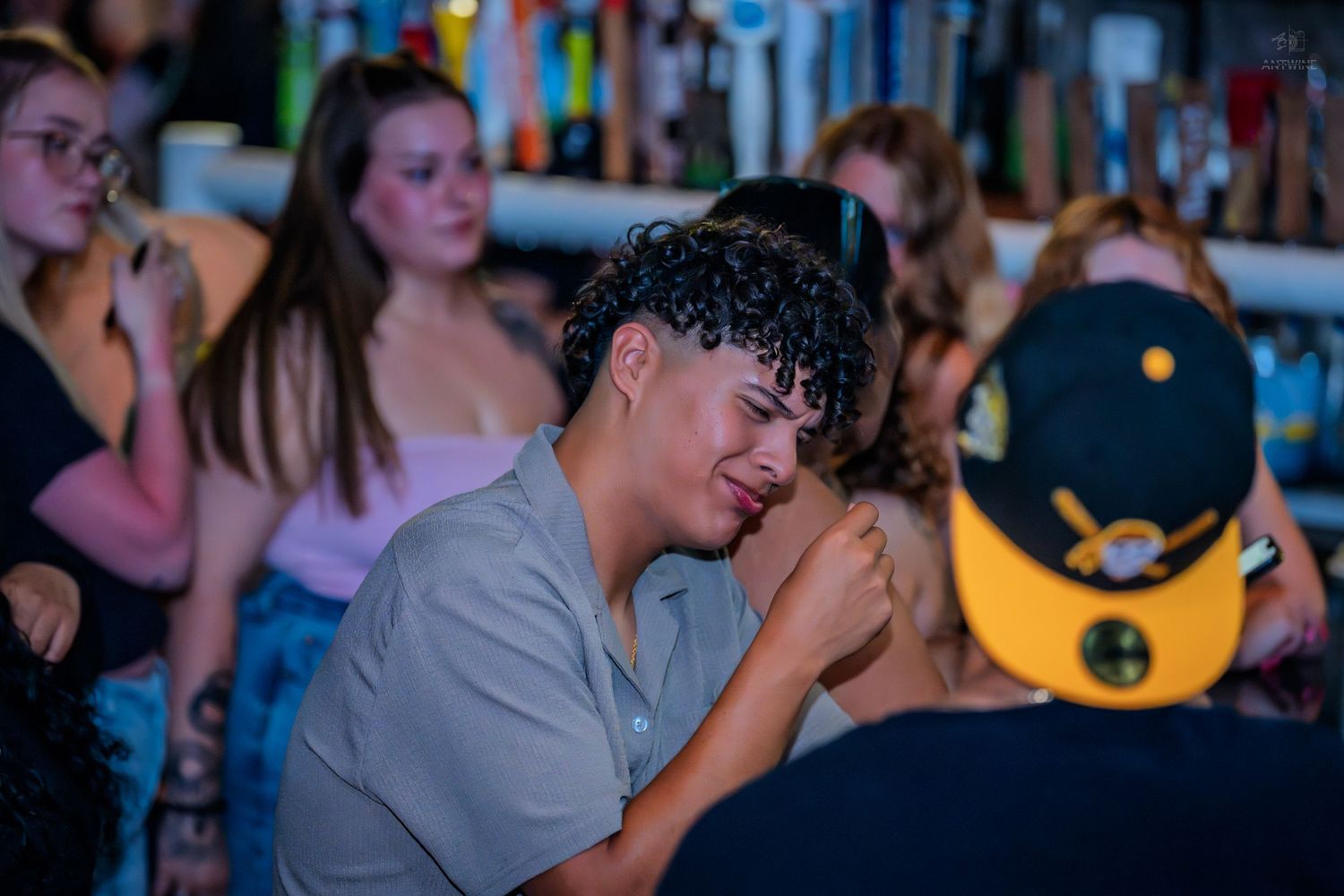 Young man with curly hair laughing at a crowded bar event.