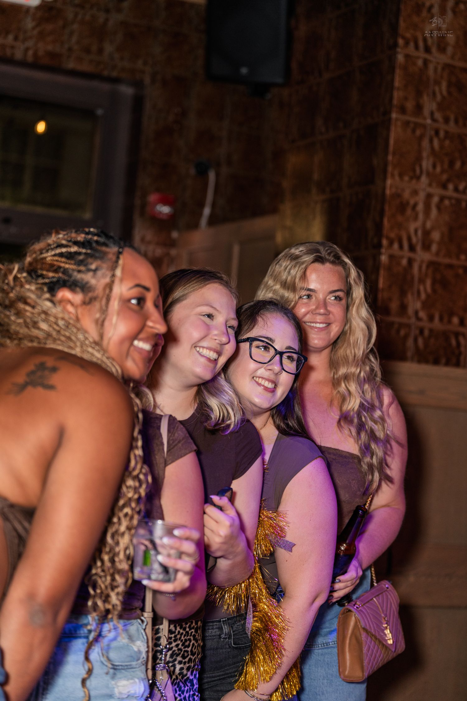 Four smiling women posing together under purple lights at a lively nightclub or bar event.