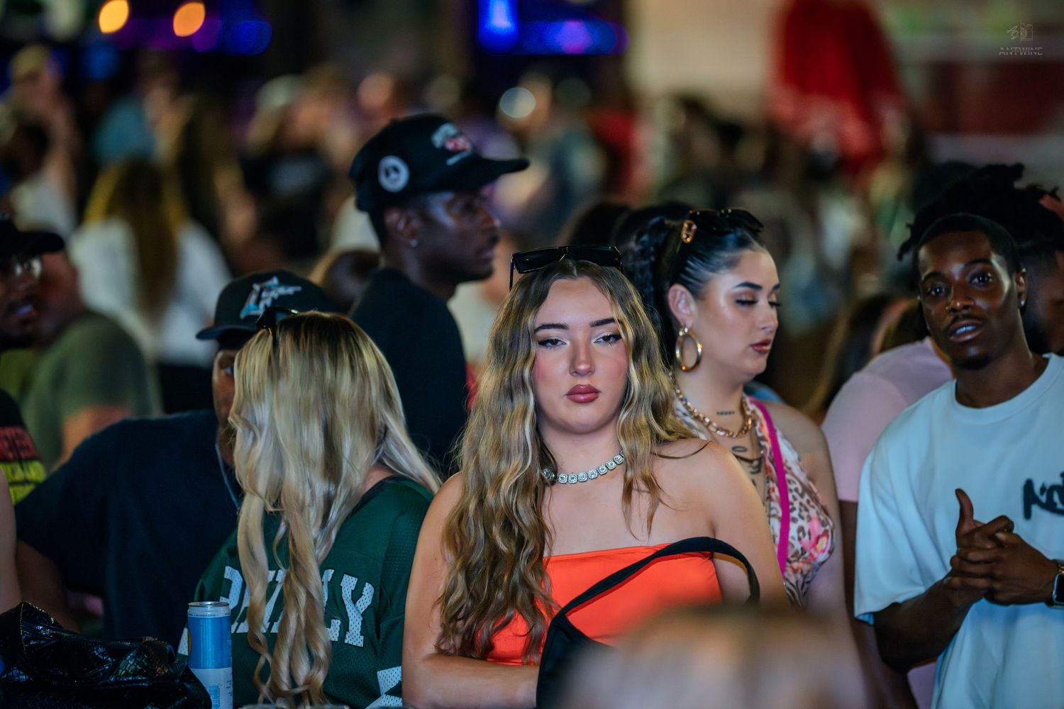 Young woman in orange top standing in crowd at outdoor nighttime party.