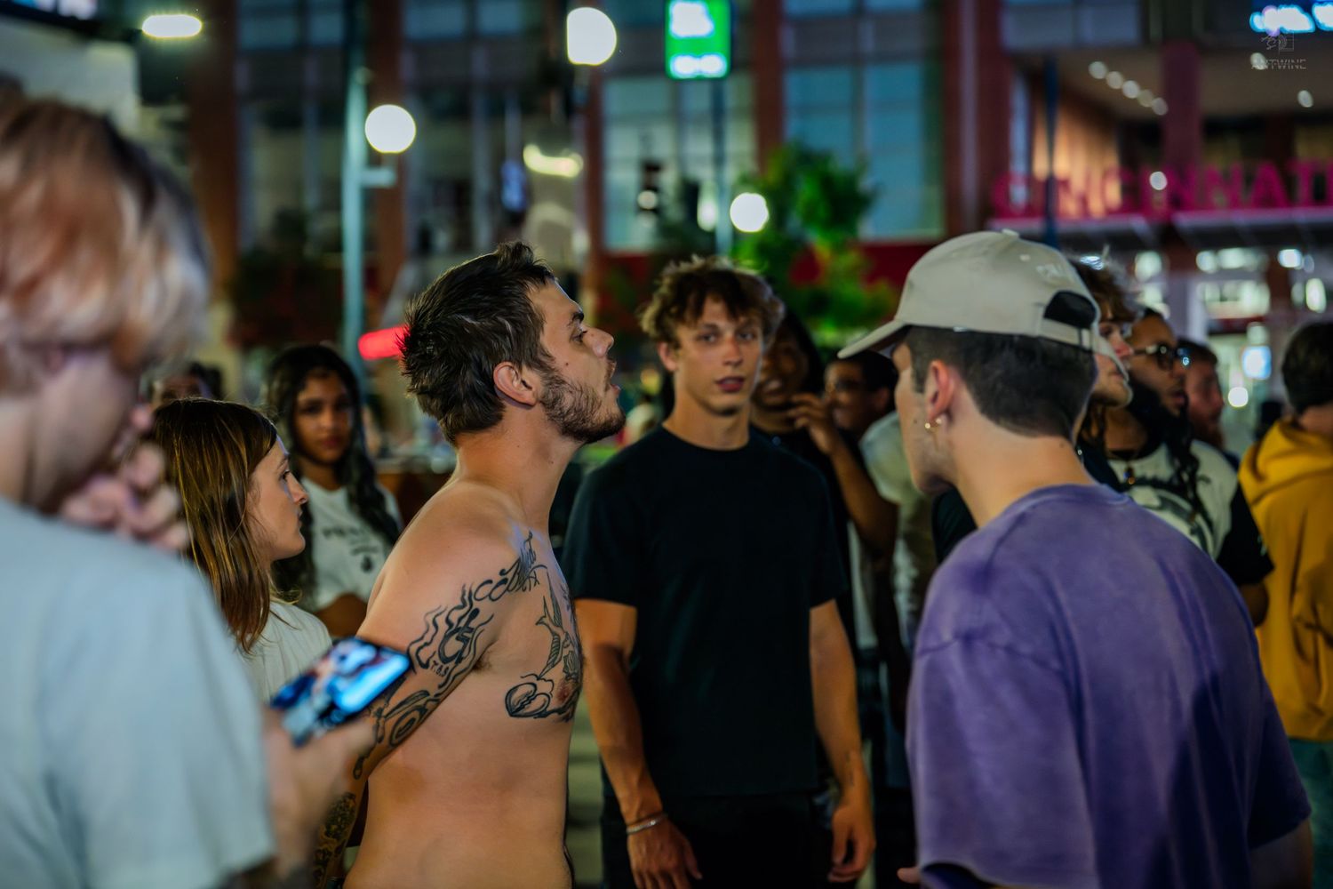 Group of young adults gathered on busy city street during nighttime event.