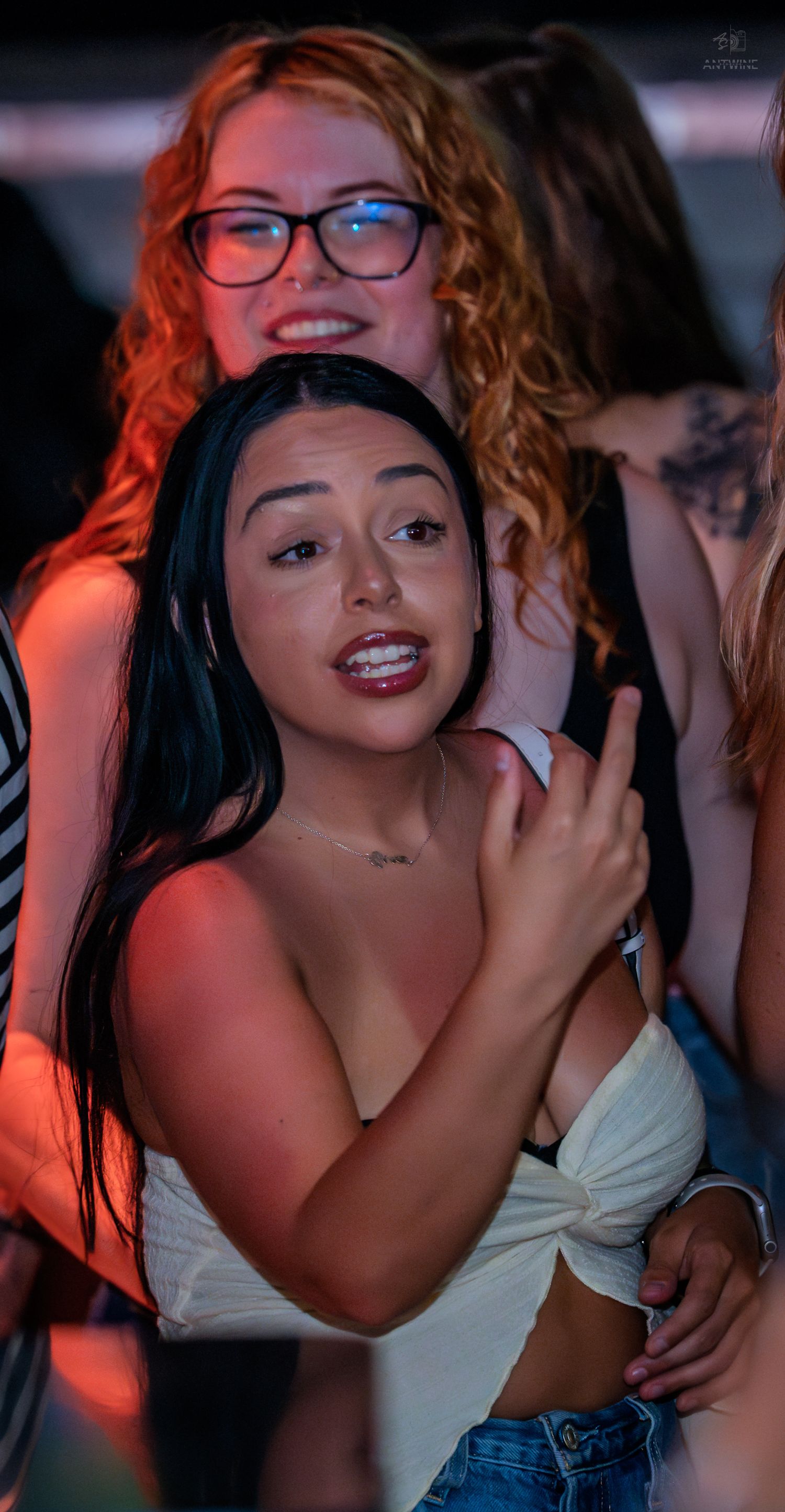 Young woman with dark hair in white crop top enjoying a lively nightclub event.
