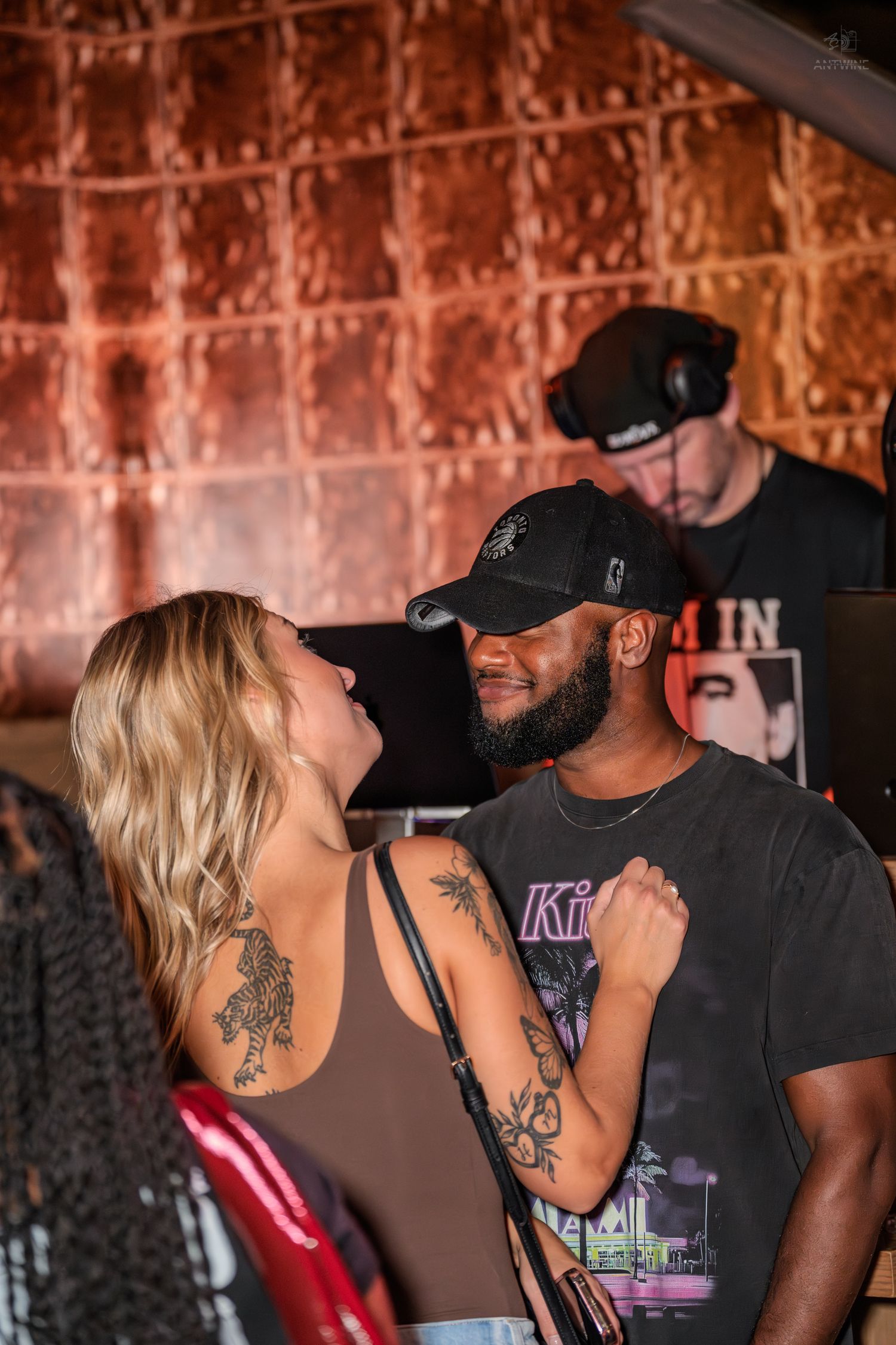 A couple shares an intimate moment at a nightclub with a DJ performing in the background.