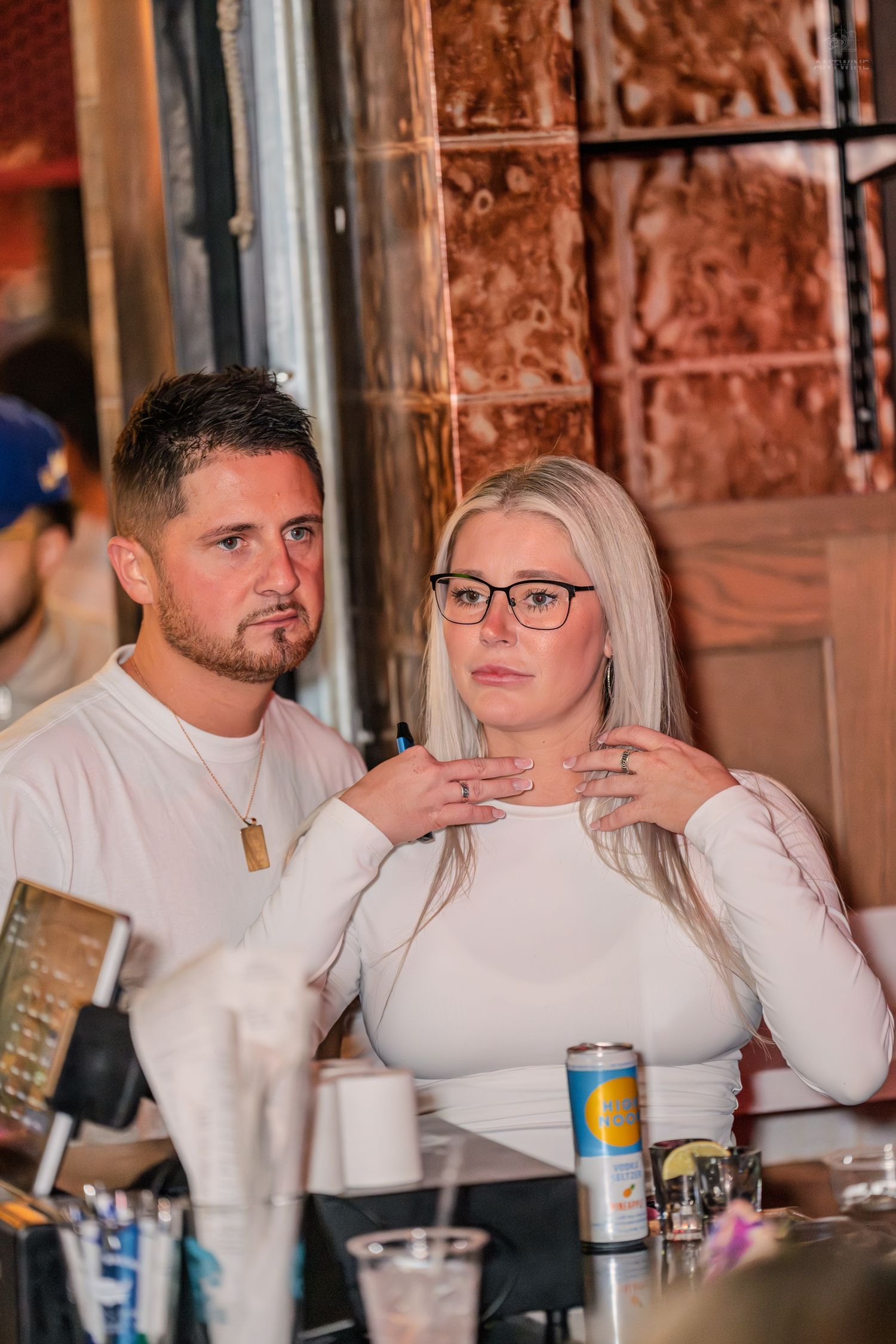 Couple in matching white outfits sitting together at a bar counter.