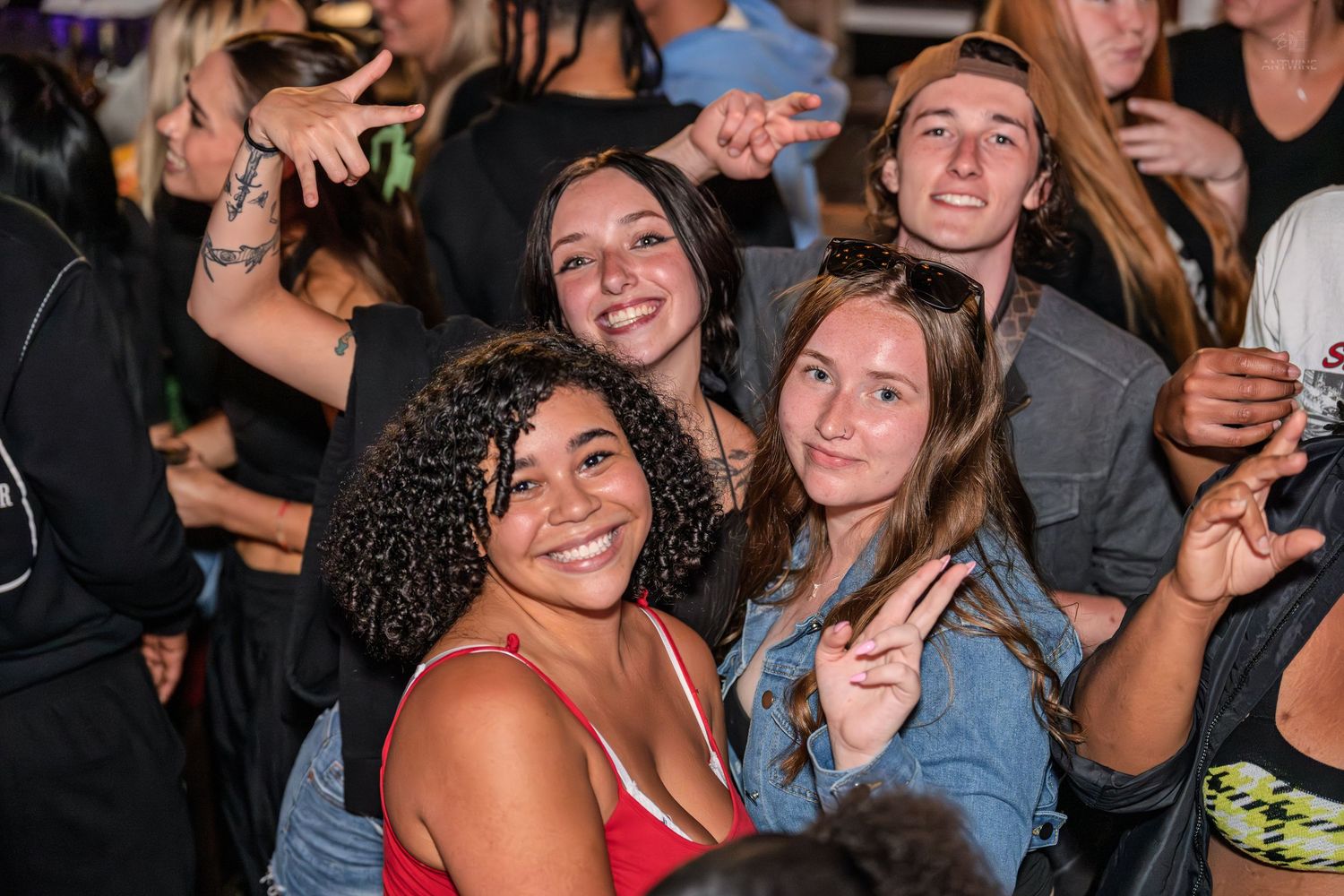 Group of happy young people flashing peace signs and smiling at a lively outdoor nighttime event.