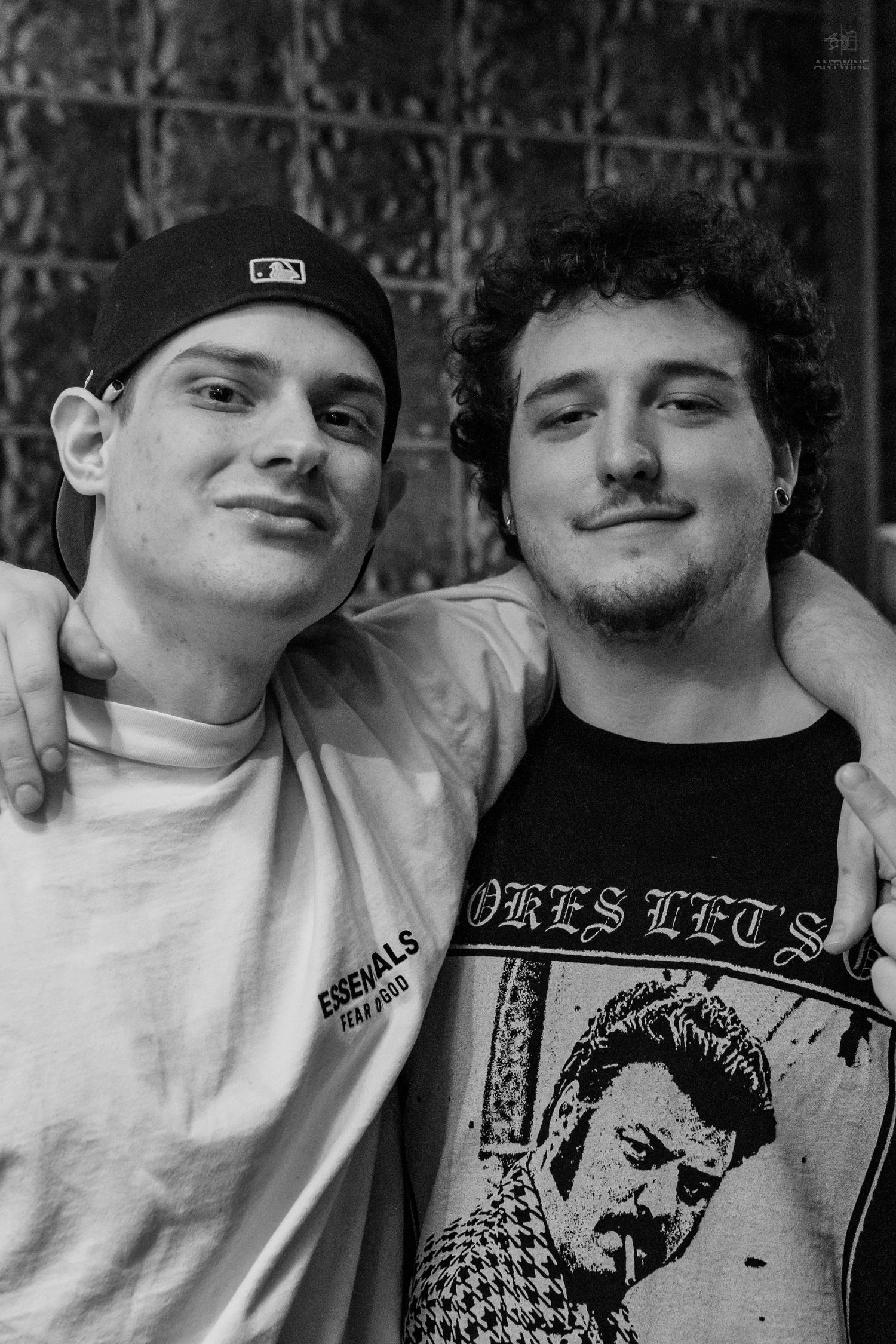 Black and white close-up photo of two young men smiling with arms around each other at a venue.