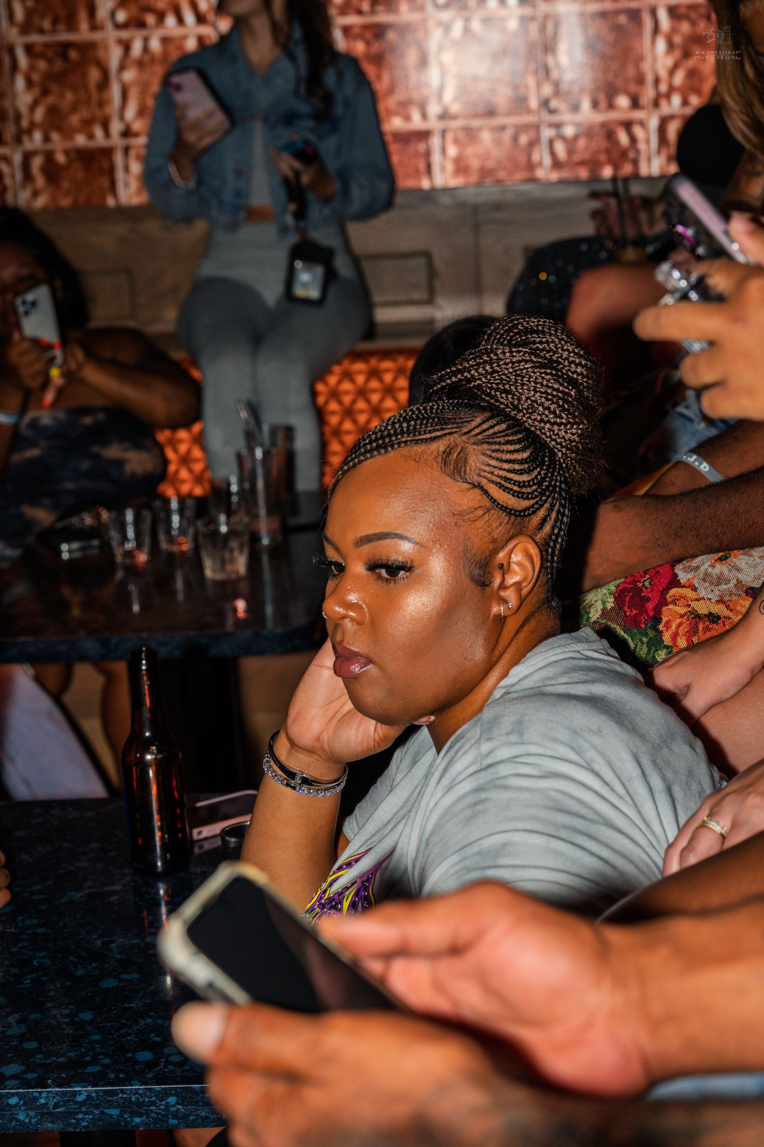 Woman with braided updo sitting at bar looking thoughtful at nightclub event.