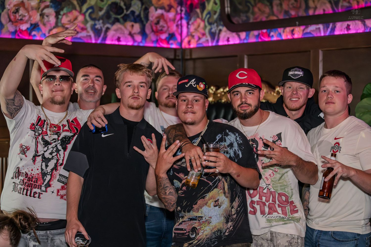 Large group of friends smiling and posing together at a colorful nightclub party.