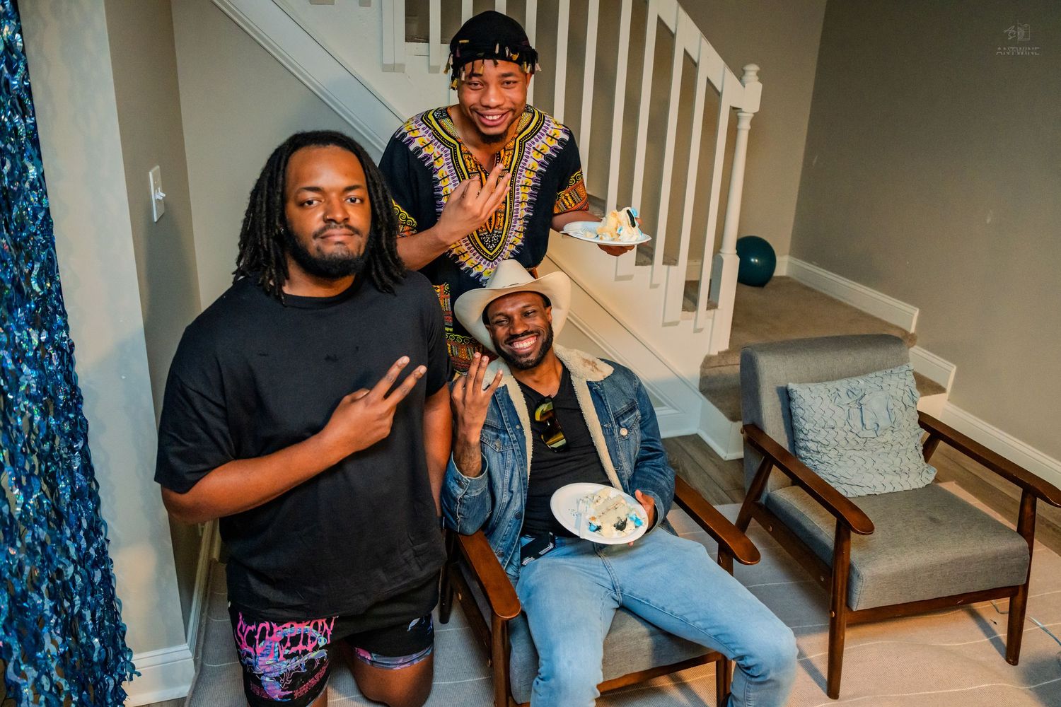 Three friends pose and smile together on a staircase at a birthday celebration indoors.