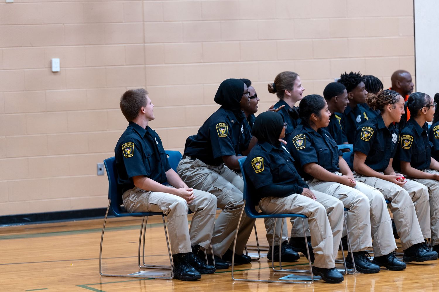 Group of young cadets in navy uniforms and khaki pants seated in rows during an indoor ceremony.