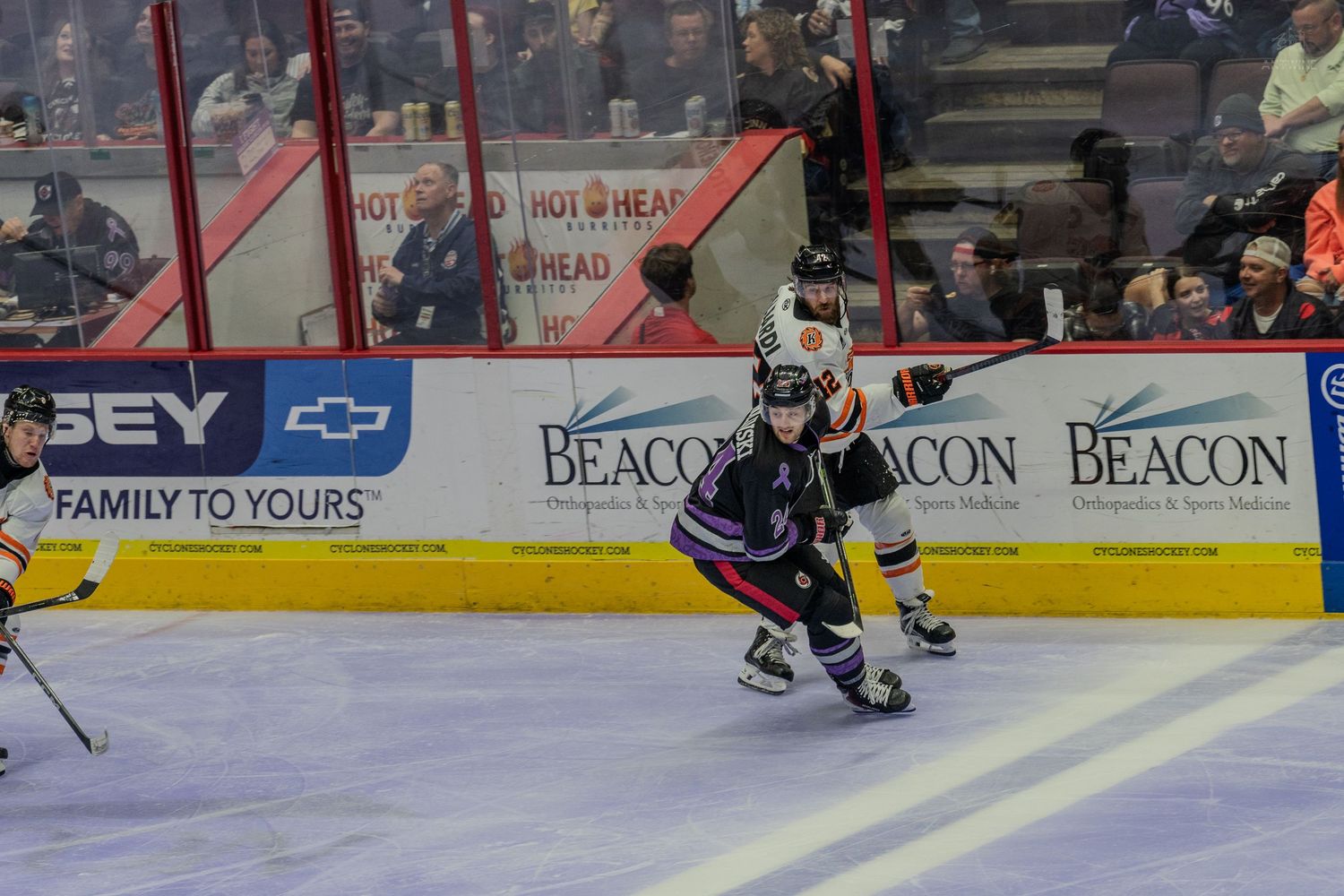 Ice hockey player in dark uniform skates along the boards past an opponent during an arena game.