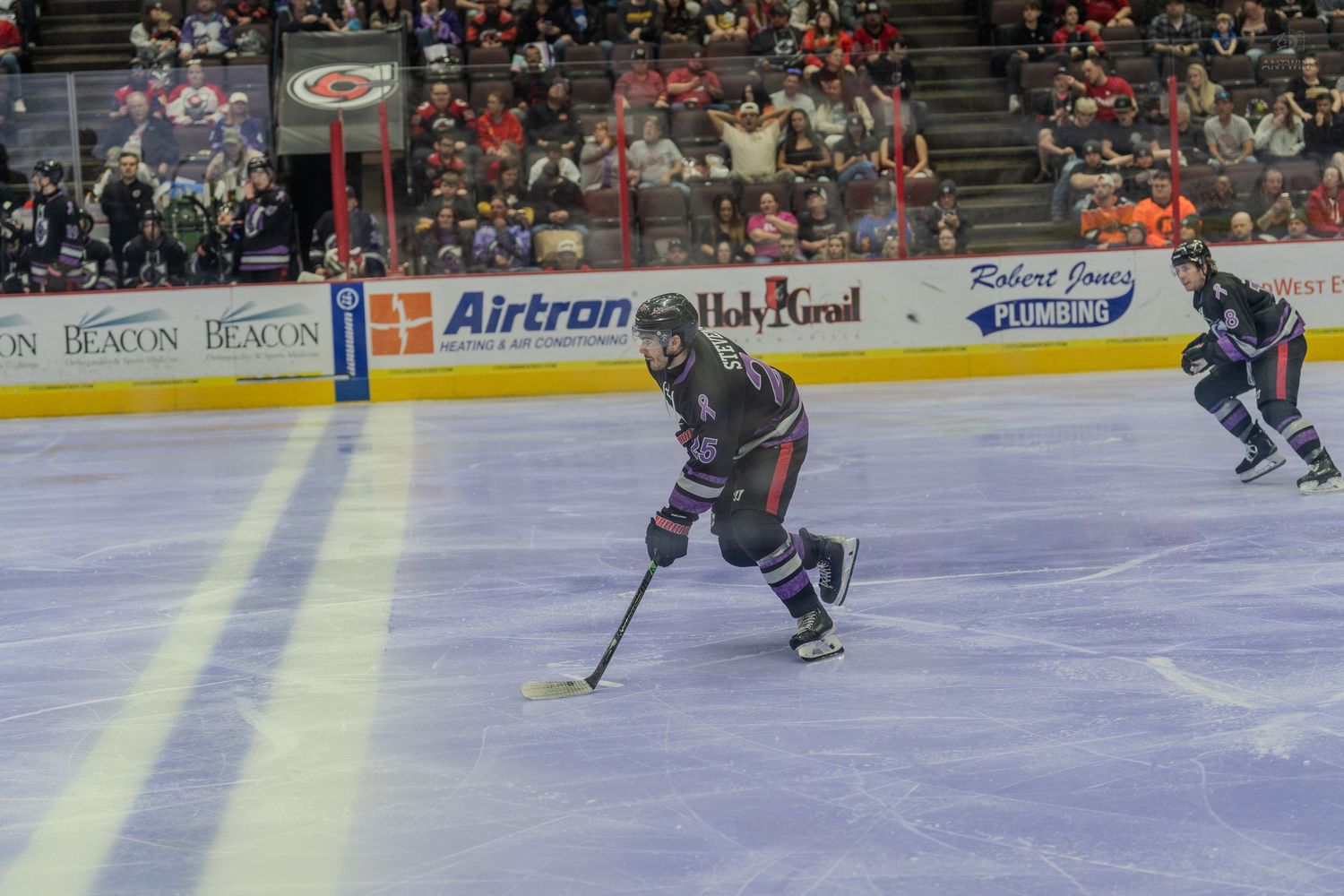 Hockey player in dark uniform skating with the puck during a minor league ice hockey game.