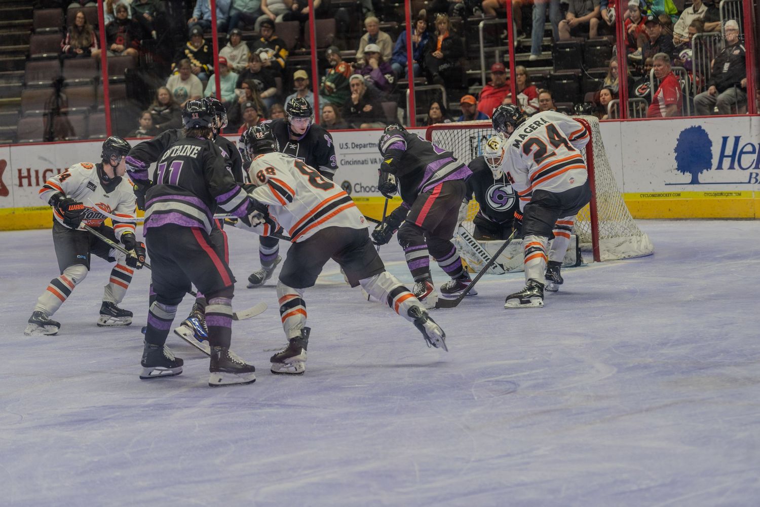 Players battle in front of the net during an intense minor league hockey game action sequence.