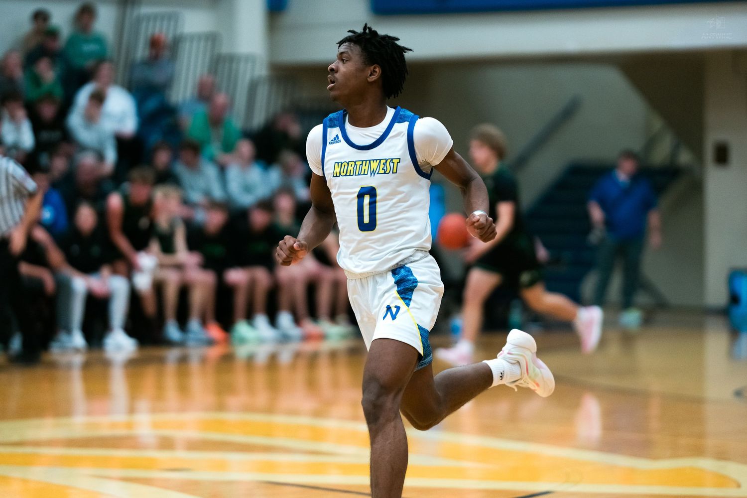 Player in blue number 0 jersey runs on basketball court before packed gymnasium crowd.