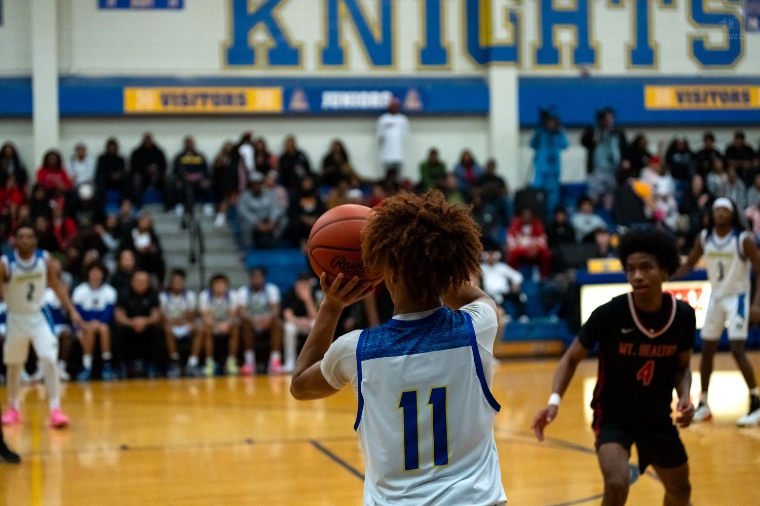 Player #11 in blue Knights uniform prepares to shoot basketball during high school game.