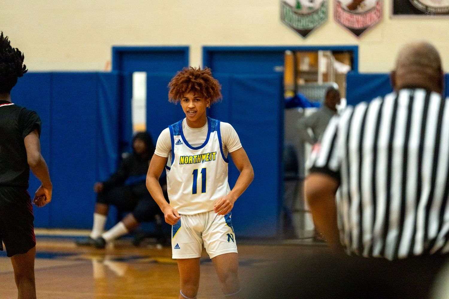 High school basketball player wearing number 11 white uniform stands near a referee during a game.