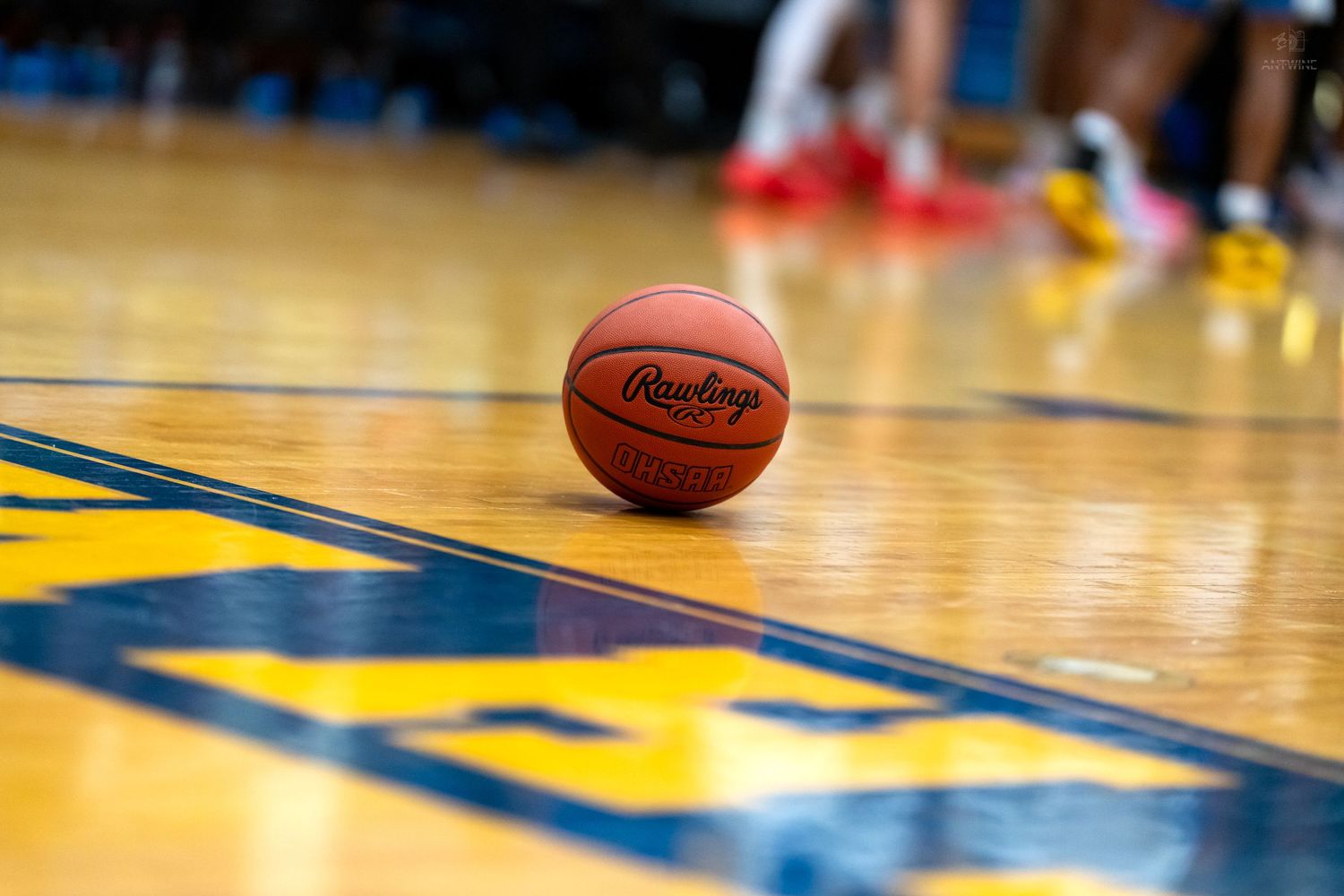 Rawlings basketball resting on a hardwood court with blue and yellow markings during a game.