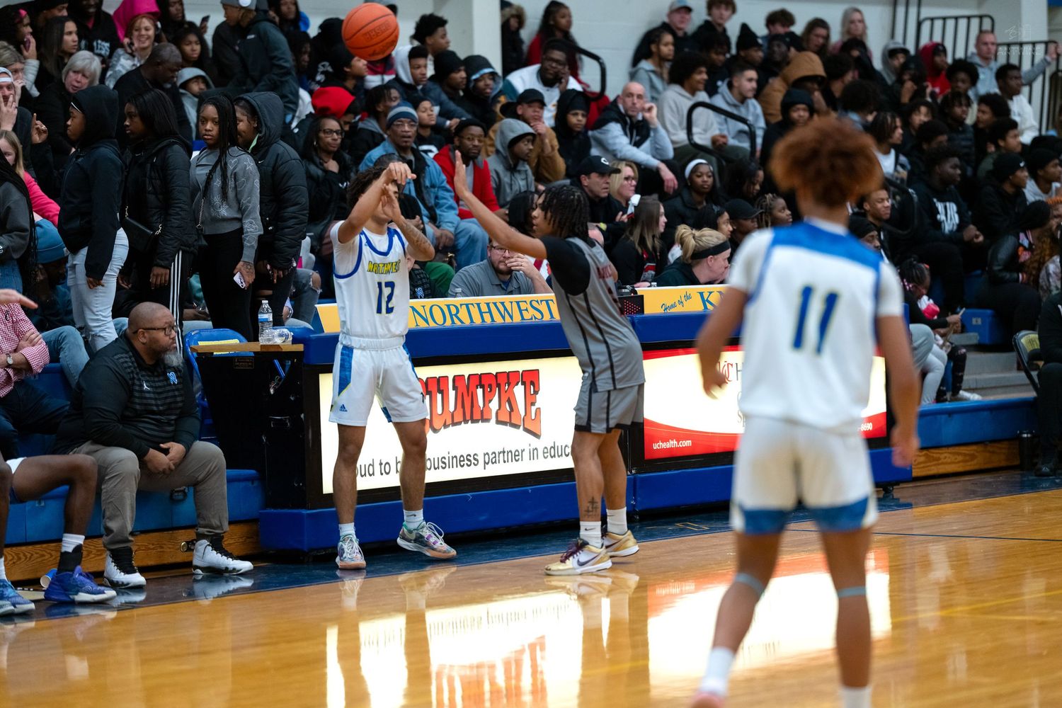 Basketball player wearing number 12 passes the ball during a high school game with a crowded sideline.