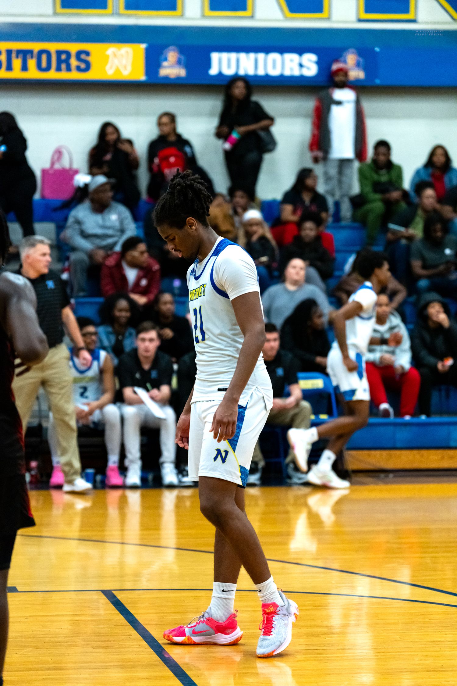 A high school basketball player wearing number 21 walks on the court during a game.