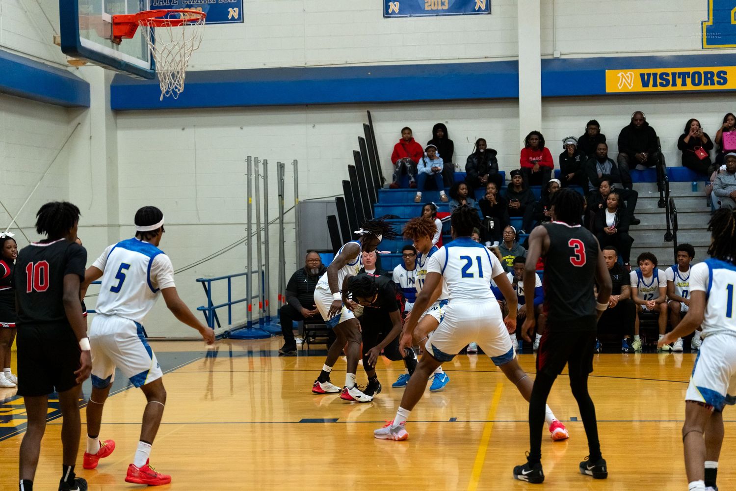 High school basketball players in blue and red jerseys compete during a crowded gym game.