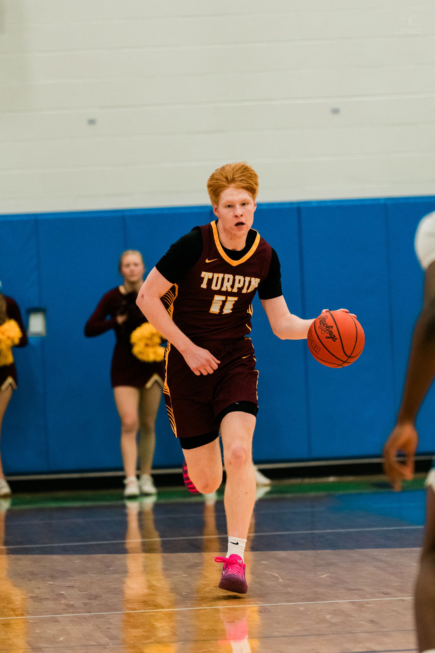 Turpin high school basketball player #11 with red hair dribbles ball down court during game.