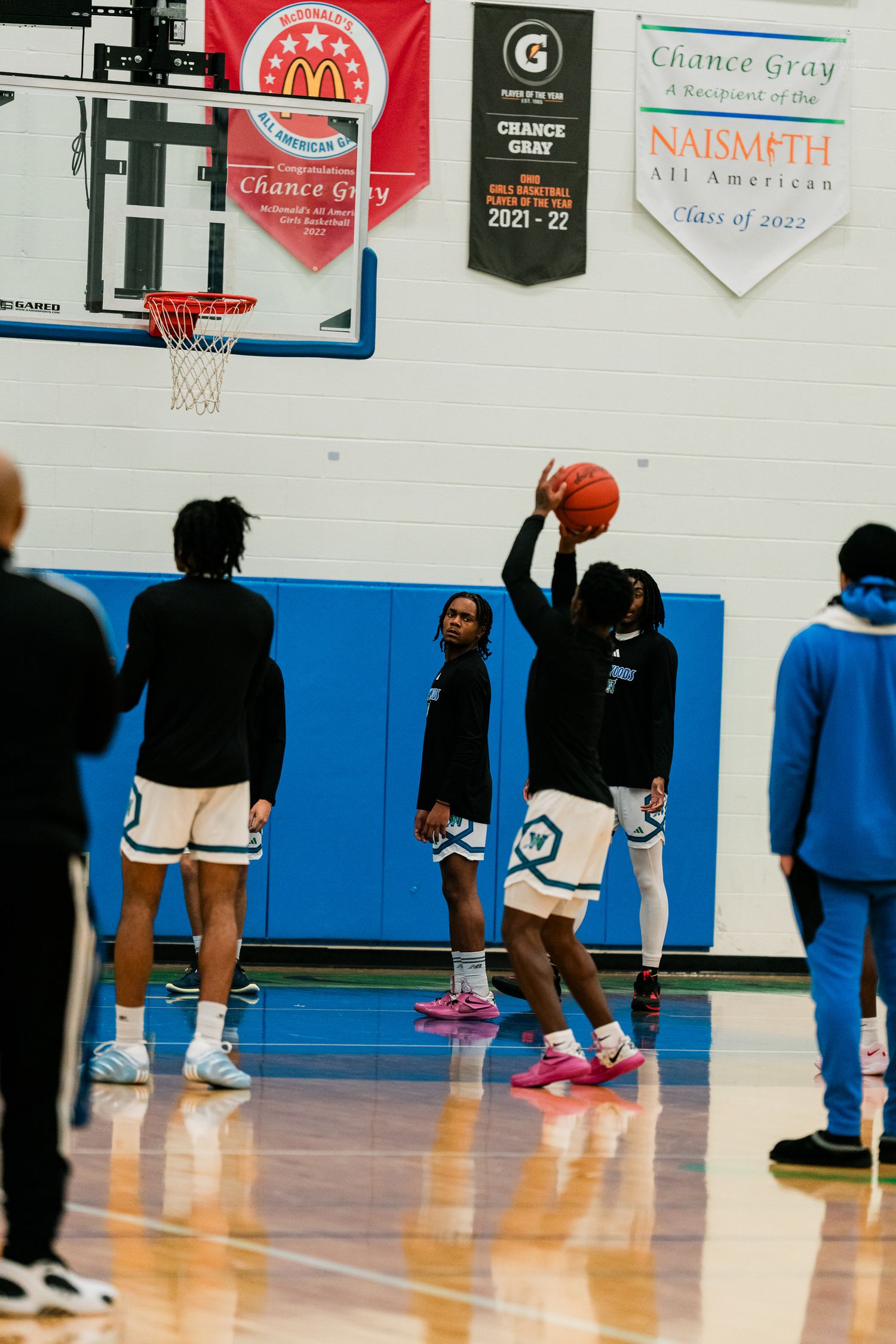 High school basketball players warm up with shooting drills under Naismith All American banners.
