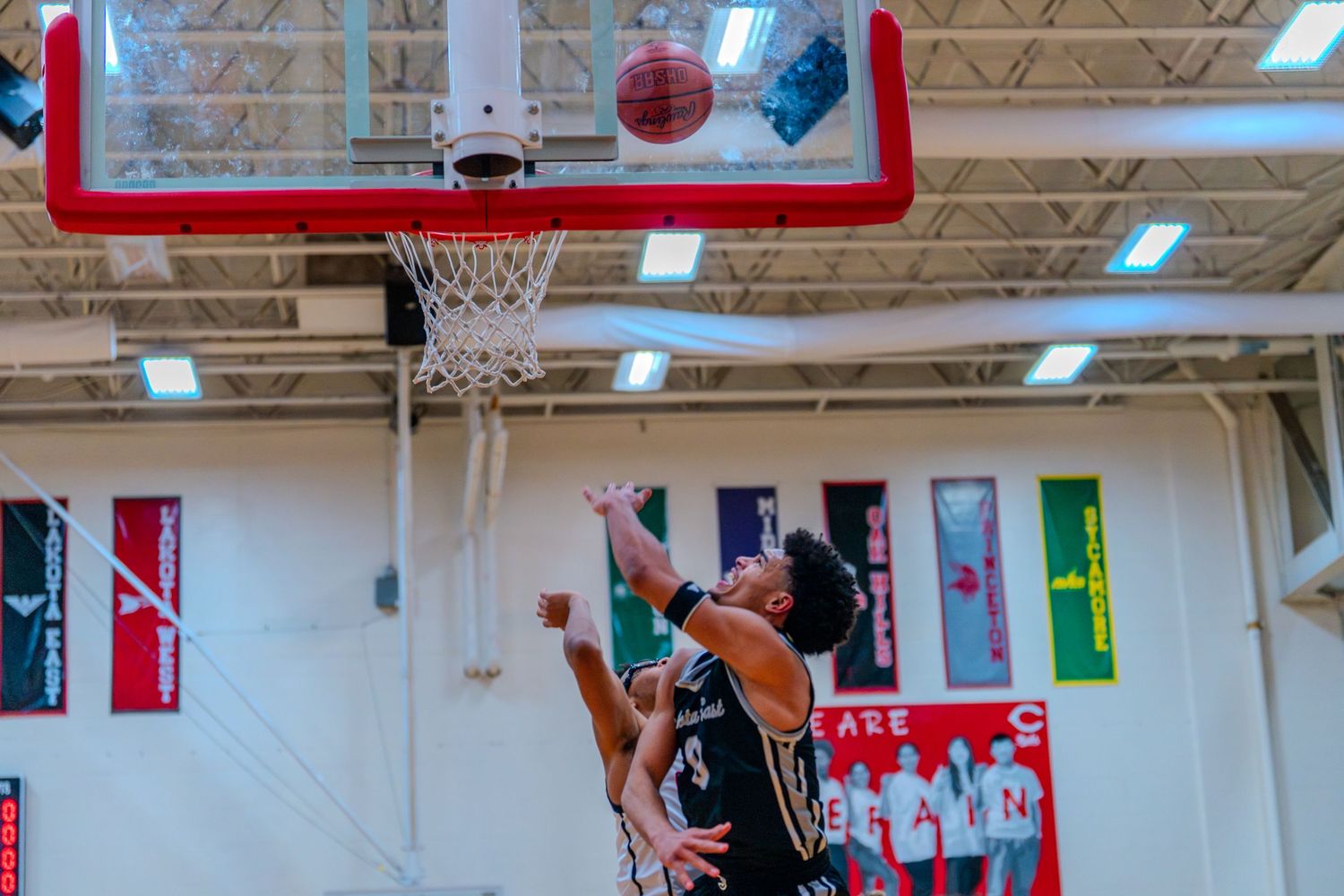 Basketball player attempts a layup at the rim during a high school basketball game in a decorated gym.