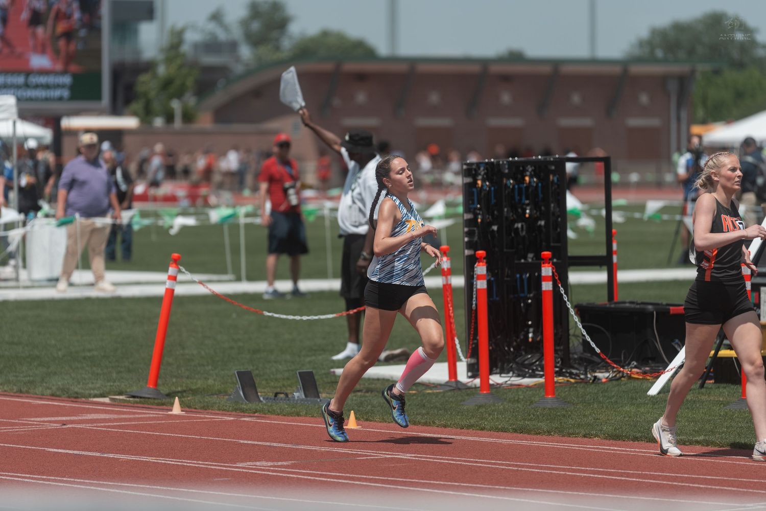 Female runner crosses the finish line at an outdoor track and field championship meet on a sunny day.