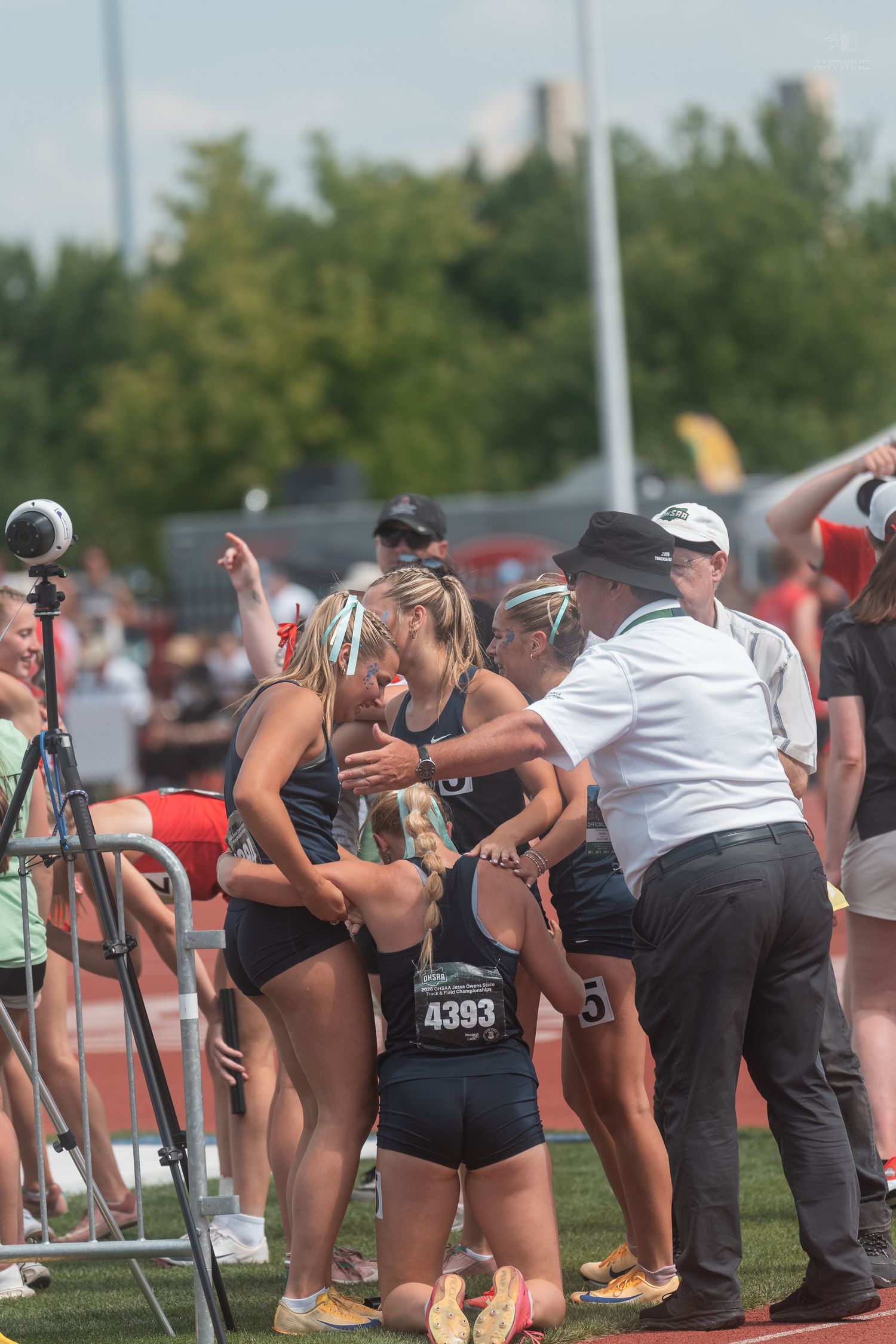 Female track athletes embracing and receiving congratulations from officials at an outdoor competition.