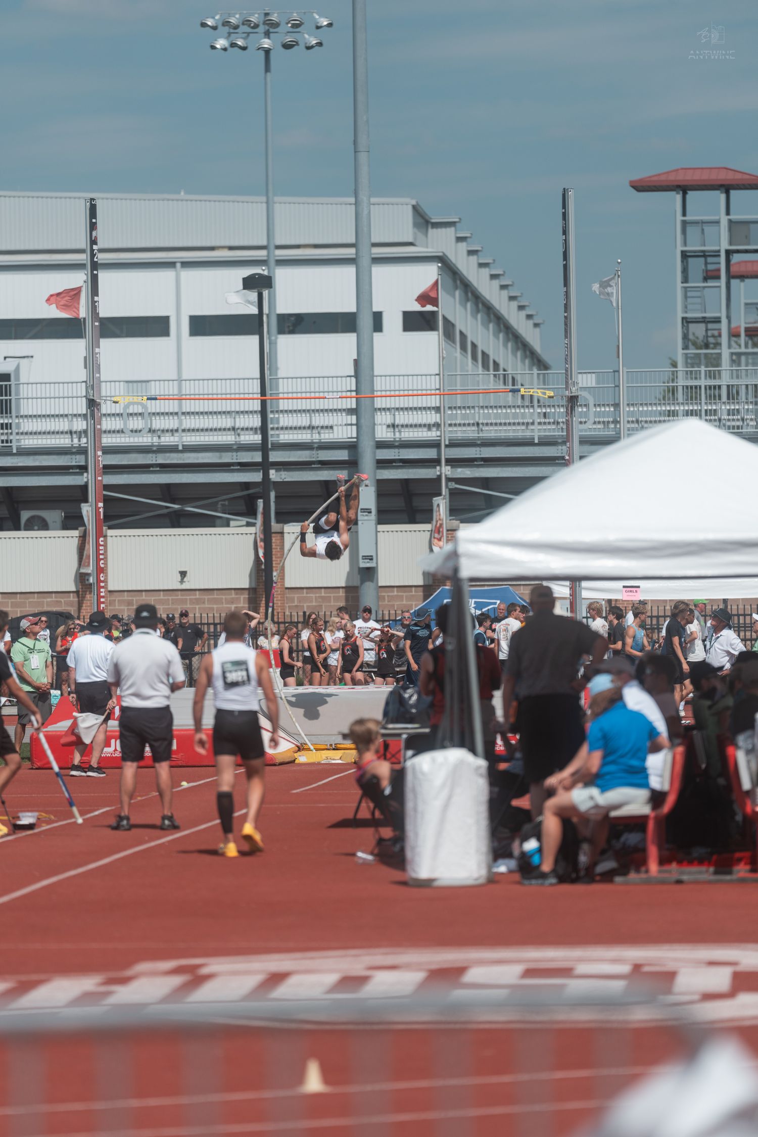 Athlete preparing for pole vault at an outdoor track meet near a large sports facility.