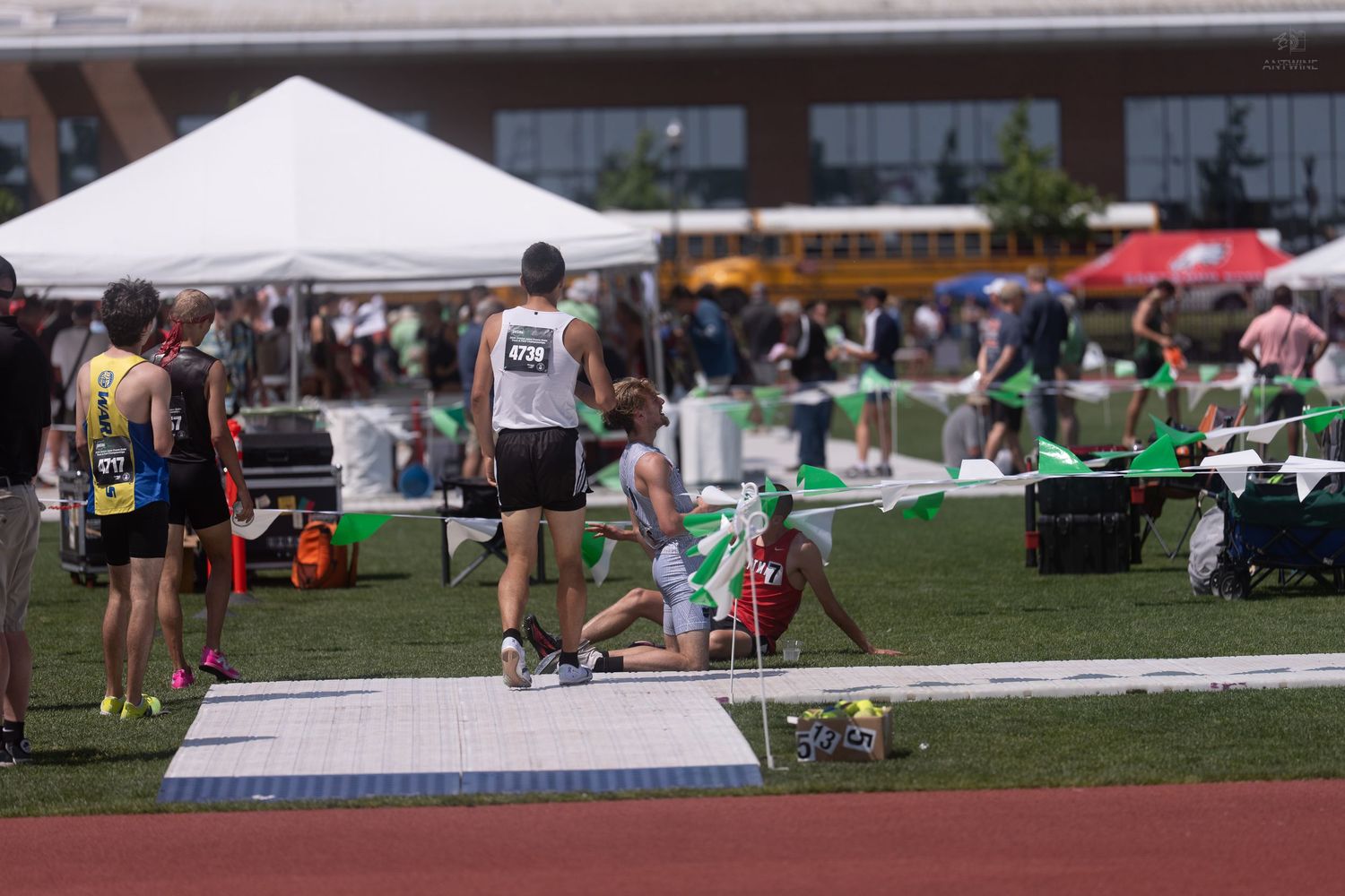 Track and field athlete rests on the ground near the long jump pit at an outdoor competition.