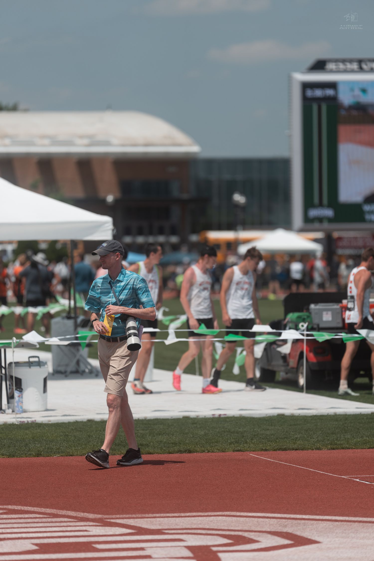Photographer with professional camera walks along red track at Jesse Owens Memorial Stadium during a track and field event.
