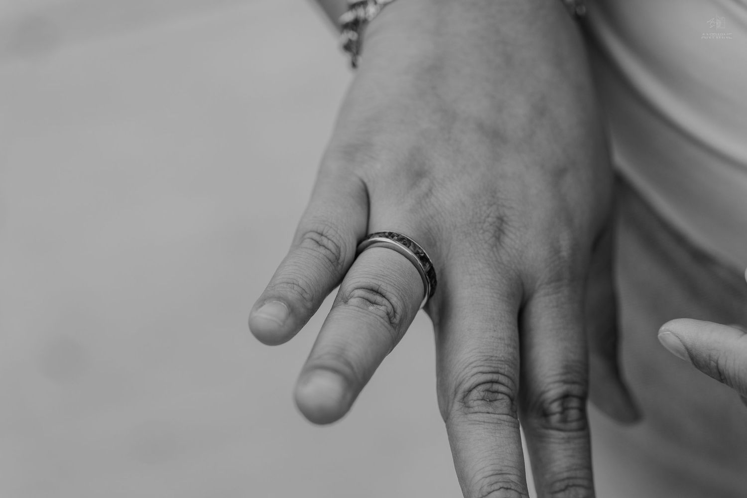 Black and white close-up of a hand wearing a simple band ring on the middle finger.
