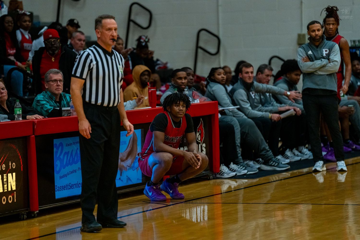 Basketball referee signals a call near the team bench during a high school basketball game.