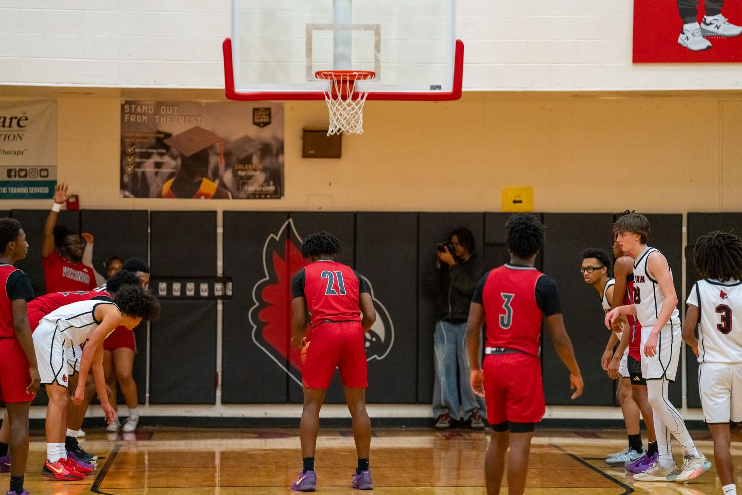 High school basketball players in red and white compete near the basket during a free throw attempt.