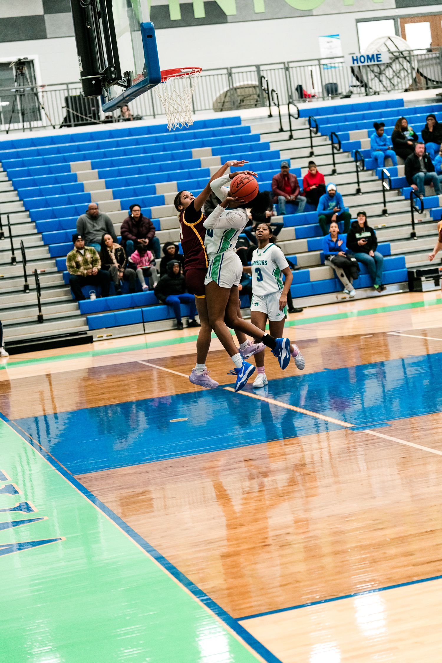 Two female basketball players battle for a rebound near the basket during a high school game.
