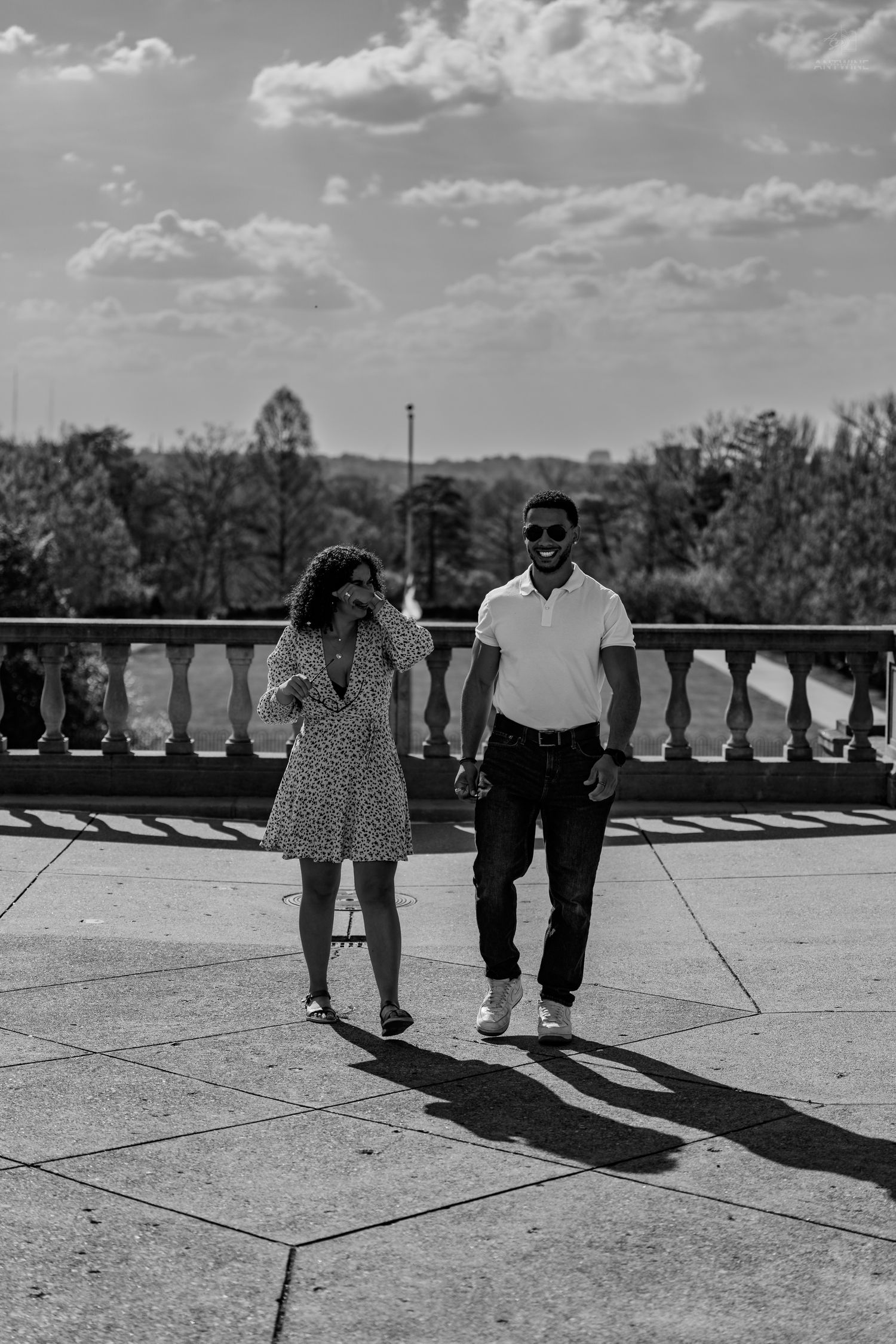 Black and white photo of a couple walking and smiling on a stone terrace under a cloudy sky.