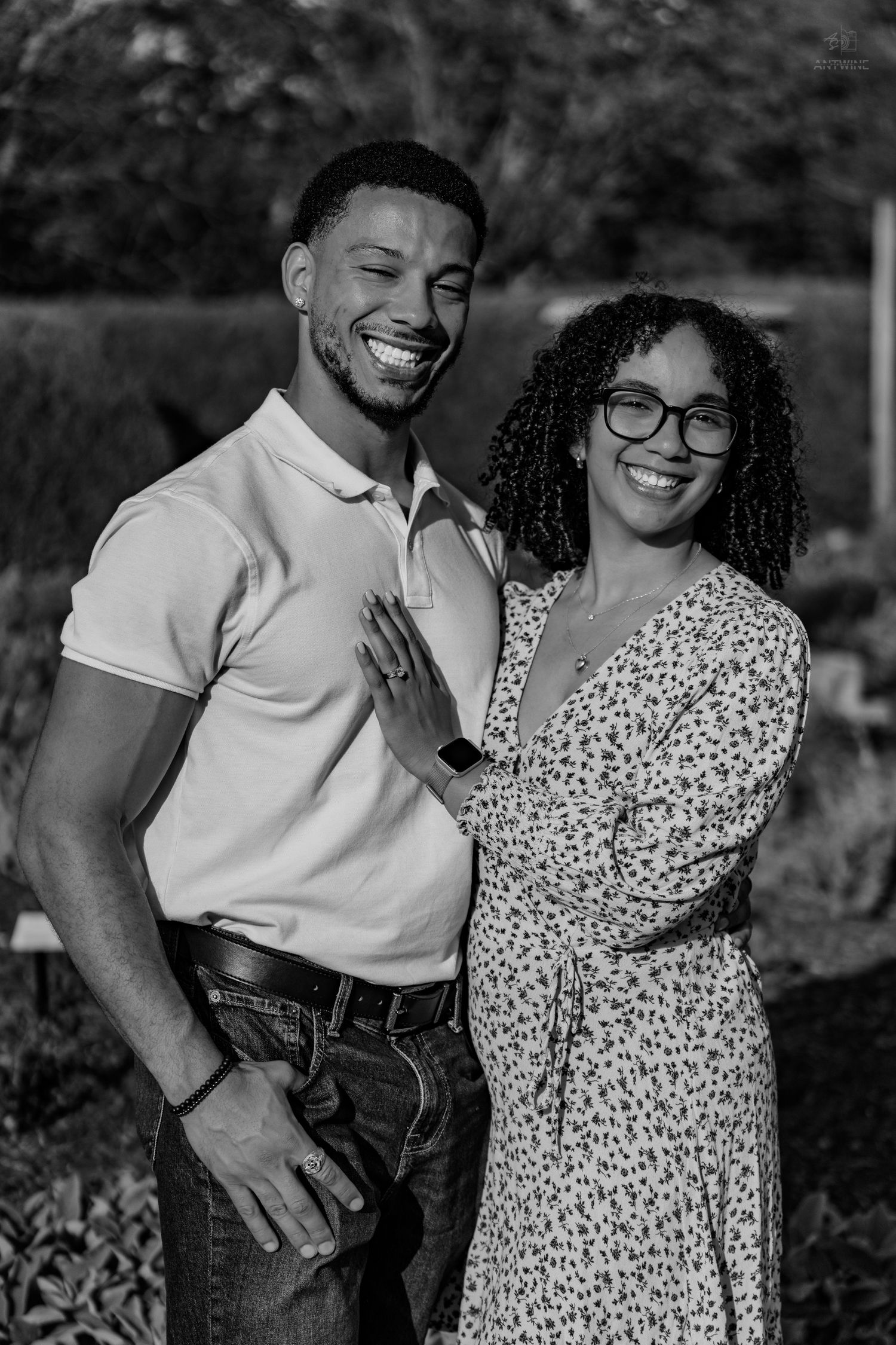 Black and white portrait of a smiling couple posing together outdoors in a garden setting.