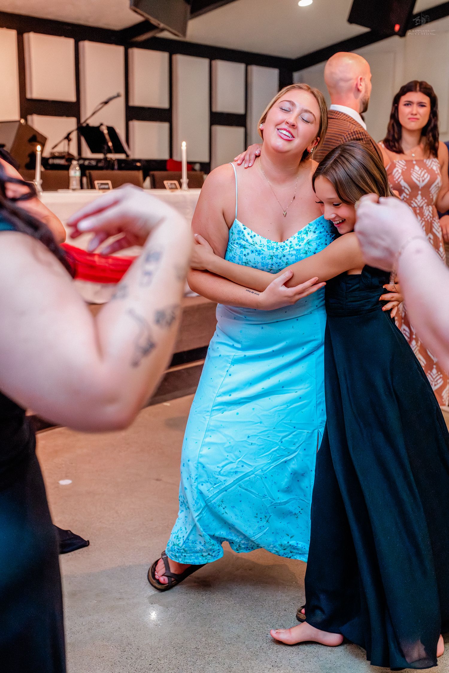 Two women in formal gowns hugging and laughing joyfully at an indoor celebration.