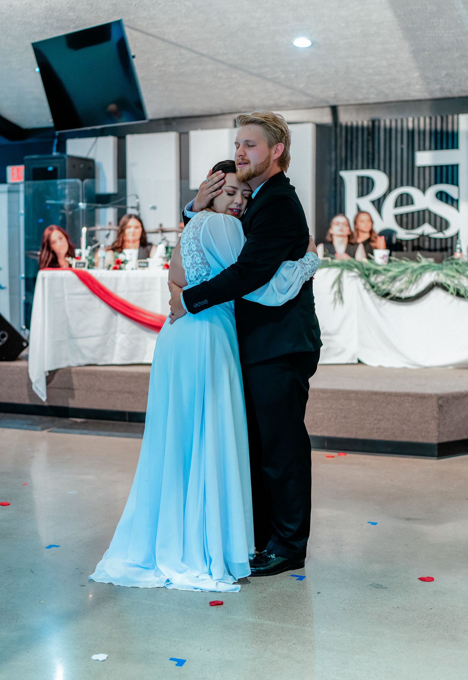 Couple sharing romantic slow dance at wedding reception, woman in light blue gown, man in black suit.