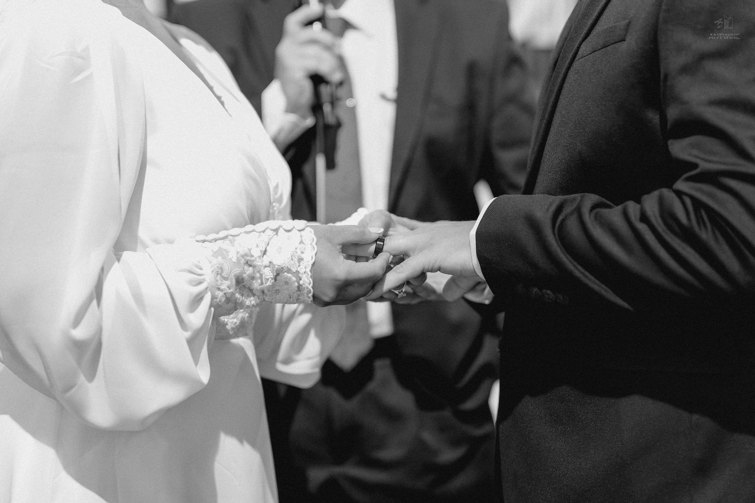 Bride and groom exchange rings during wedding ceremony in elegant black and white photo.