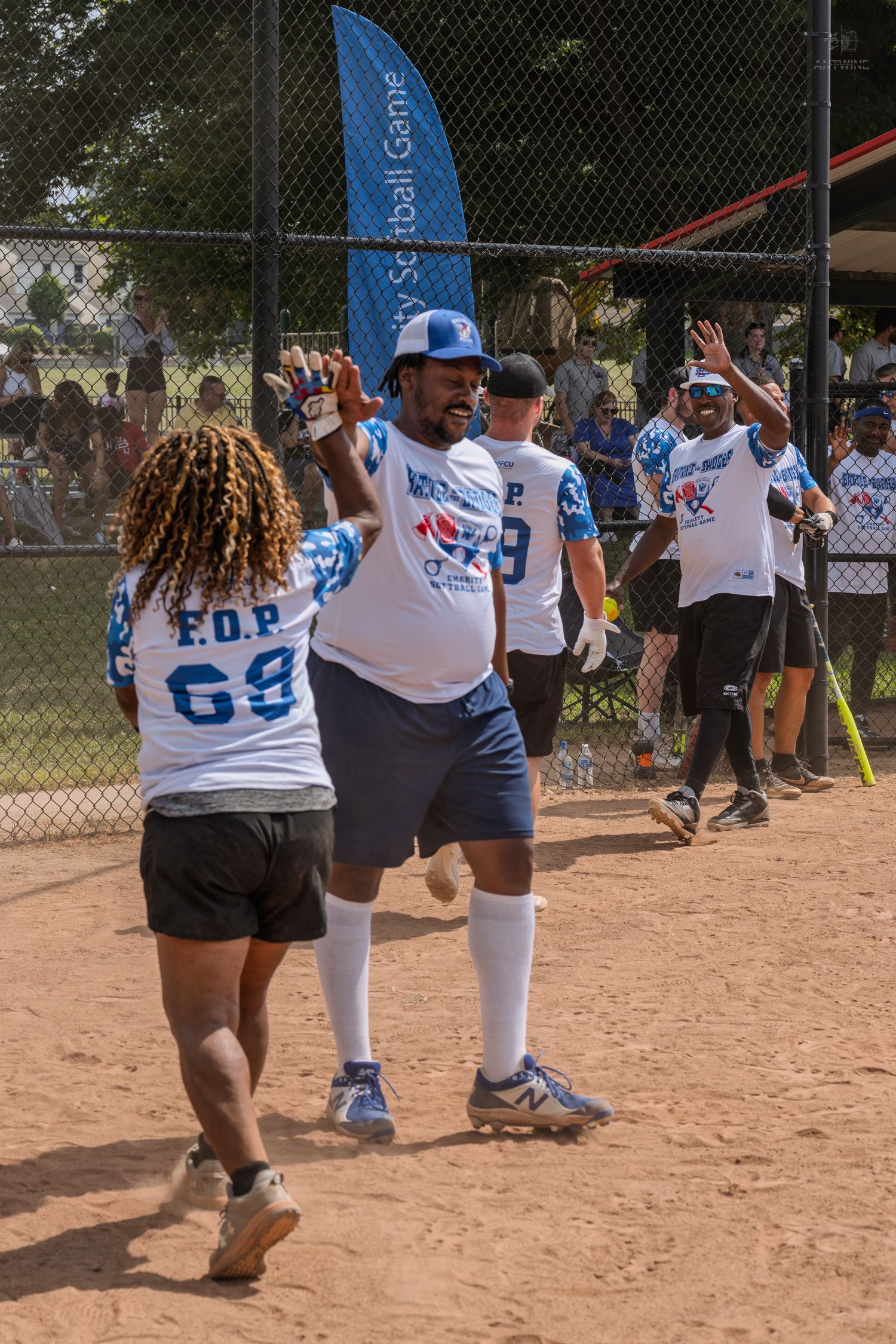 Softball players in blue FOP uniforms celebrate with high fives after scoring a run at a charity softball game.