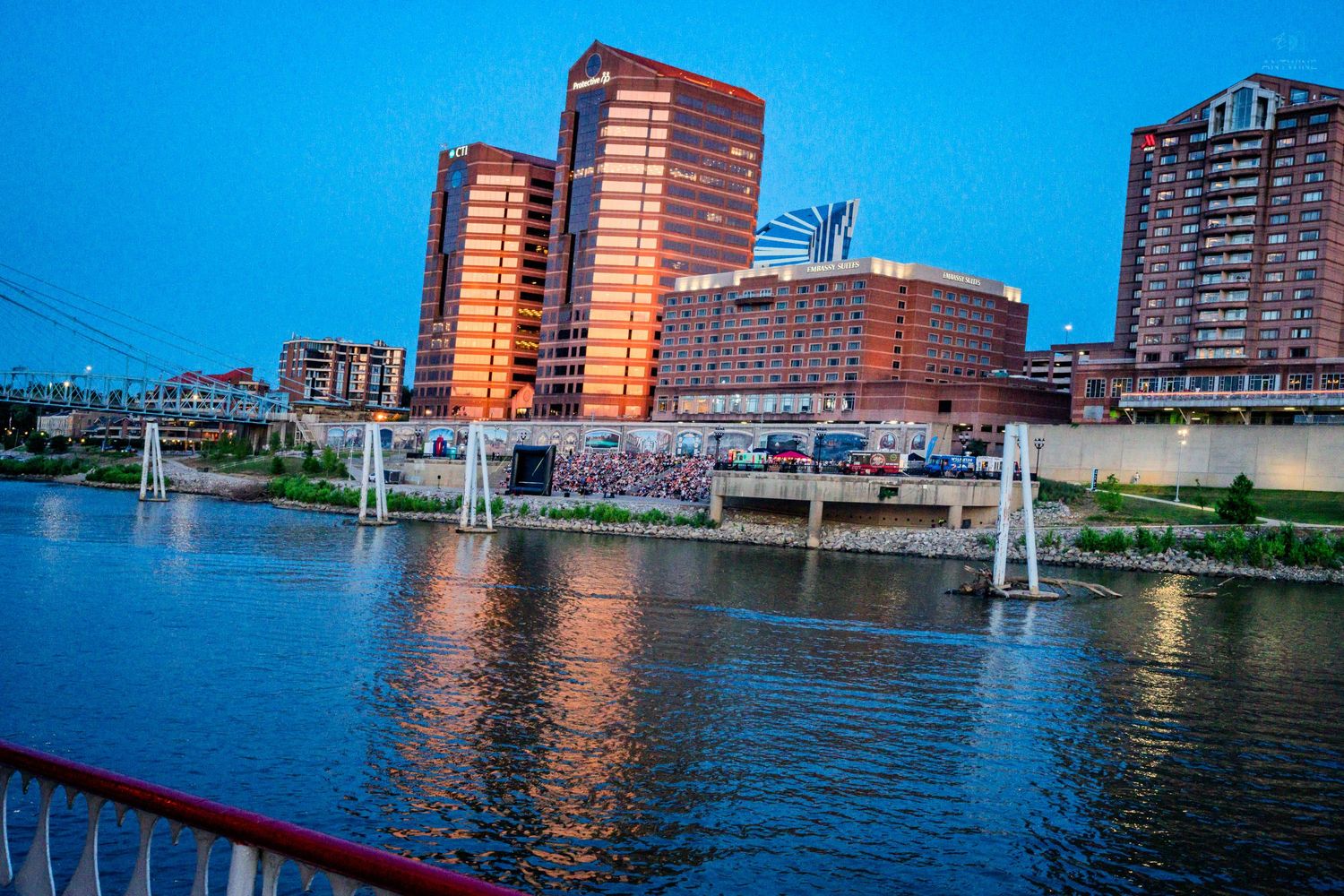 A vibrant city skyline reflects on a calm river at twilight with a bridge in view.