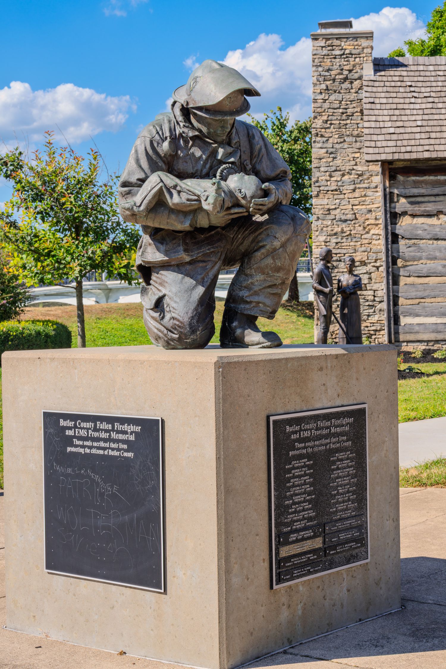Butler County Police Firefighter and EMS memorial bronze statue on stone pedestal outdoors on sunny day.