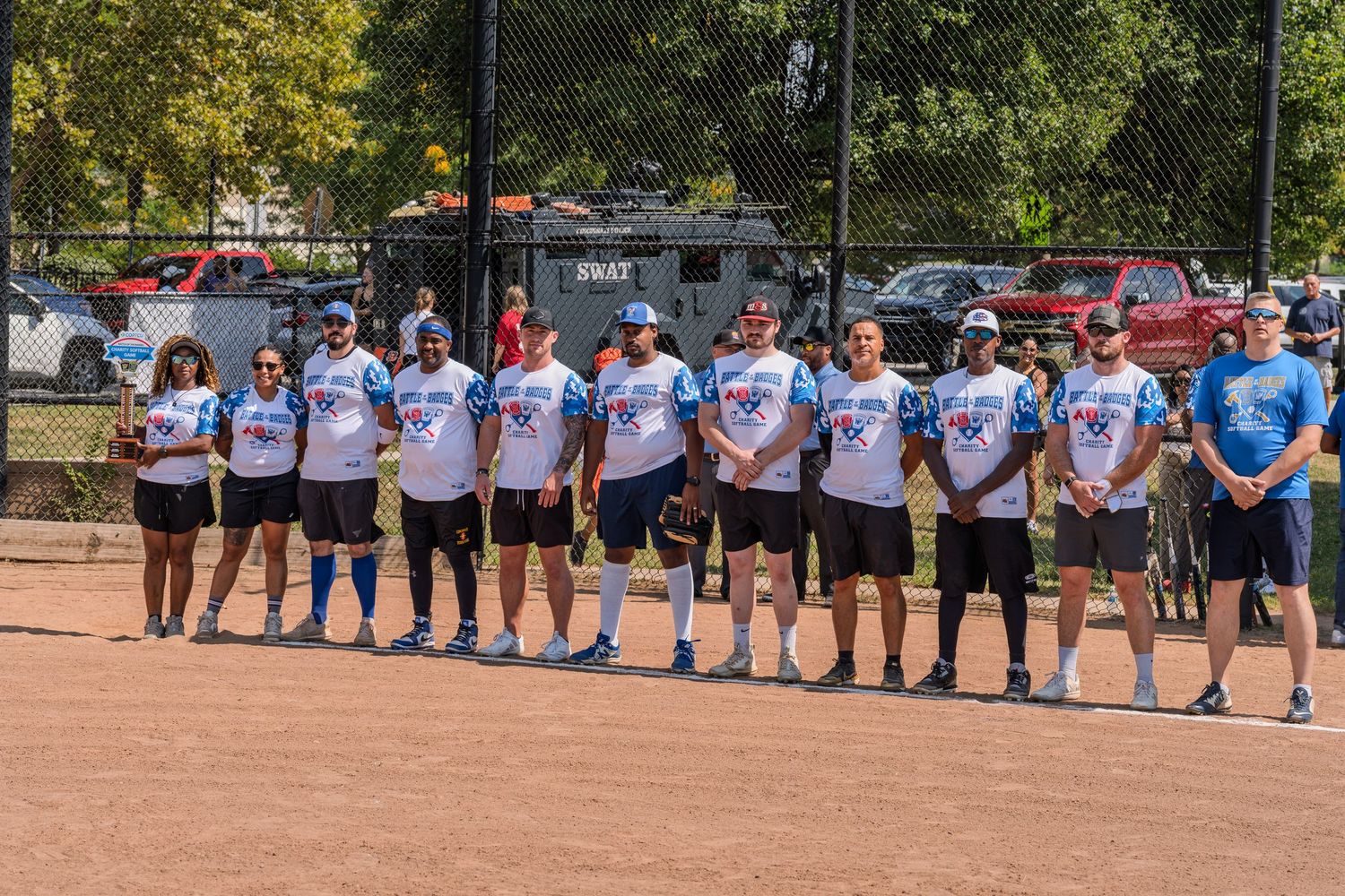 A team of softball players in matching white jerseys lines up on a field for a group photo.