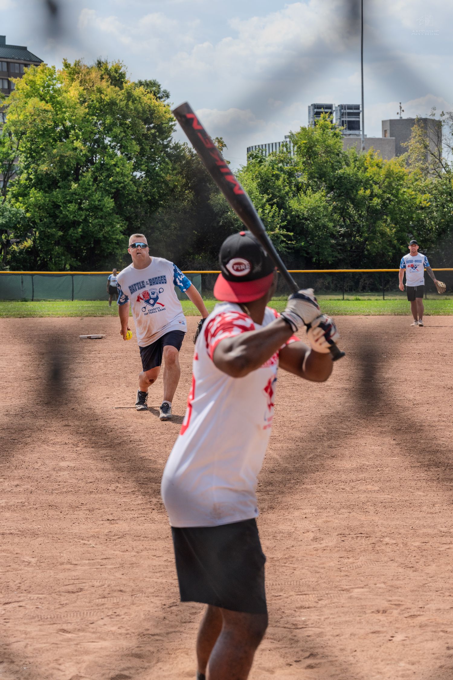 A batter prepares to swing during a Battle of the Badges charity softball game on a dirt field.