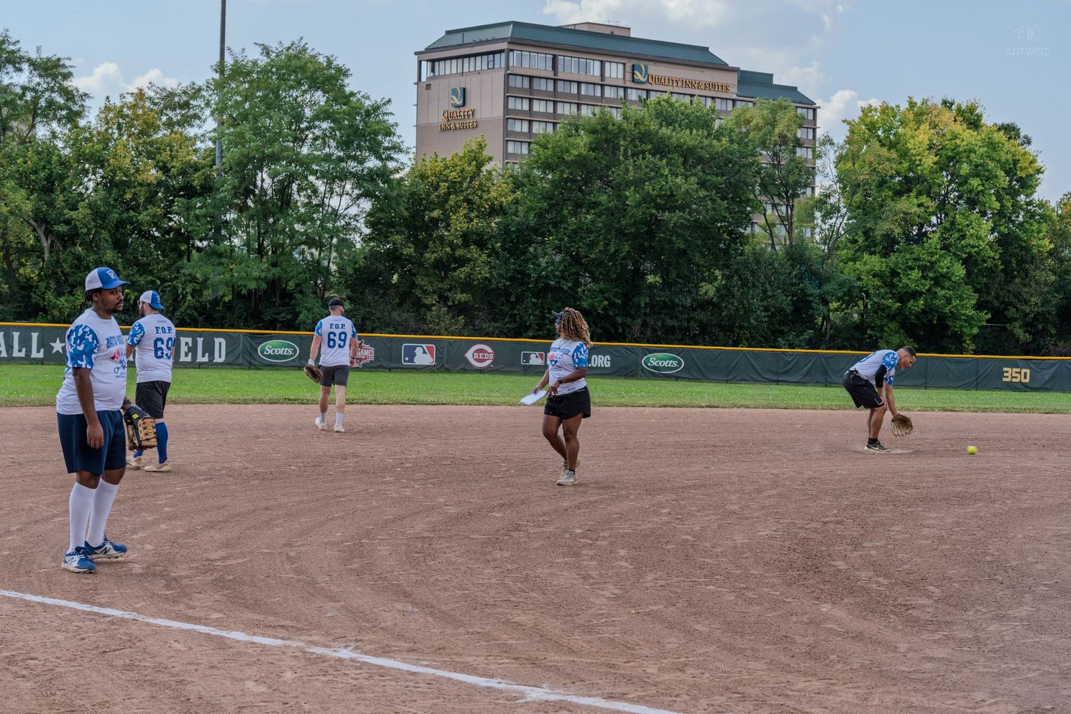 Players on a softball diamond during an outdoor game near a city building.