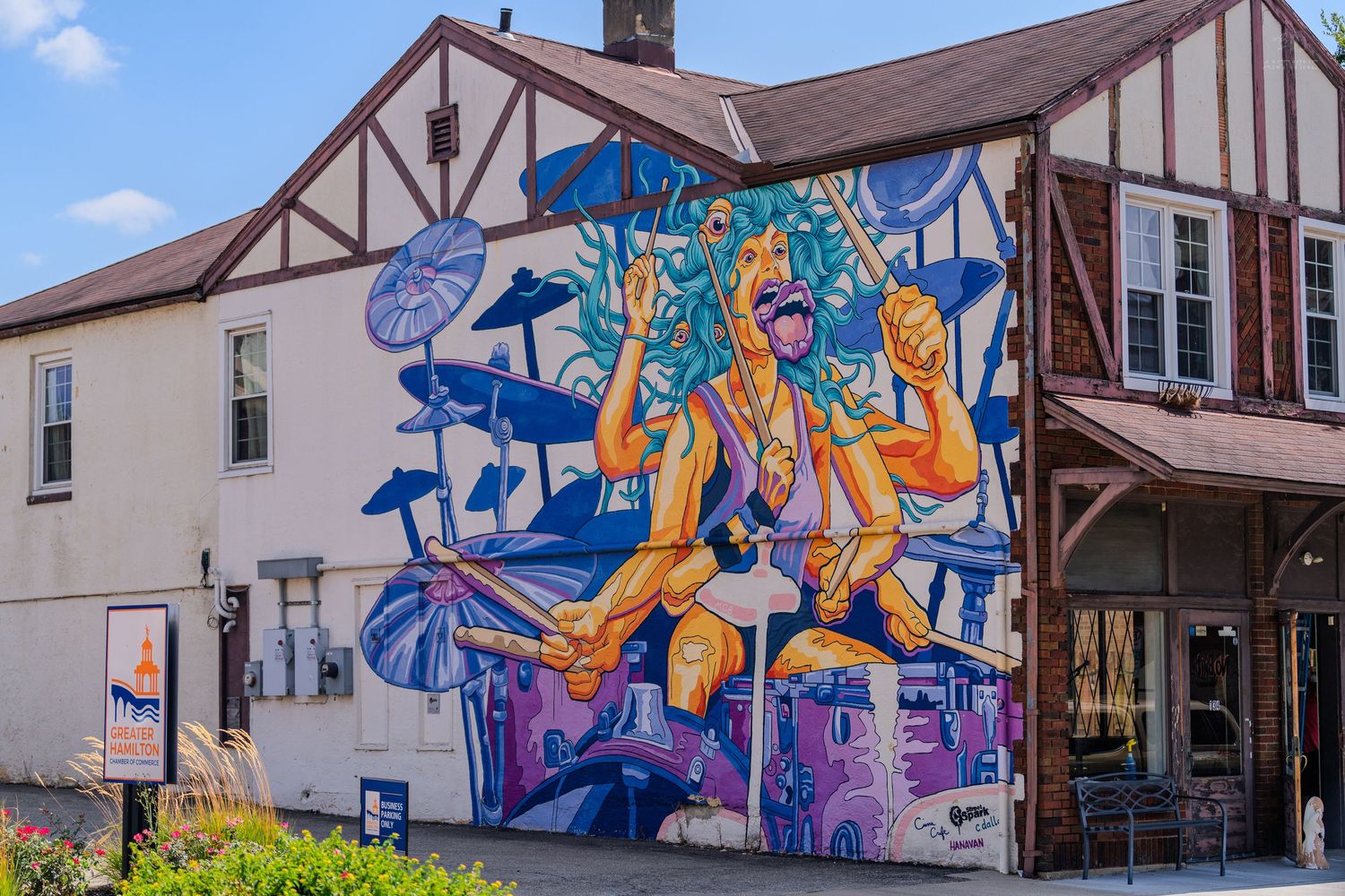 Vibrant street mural of a drummer on a Tudor-style building exterior under blue skies.