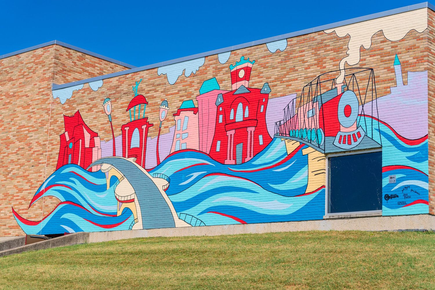 Colorful outdoor mural on brick wall featuring waves, red buildings, and a train under blue sky.
