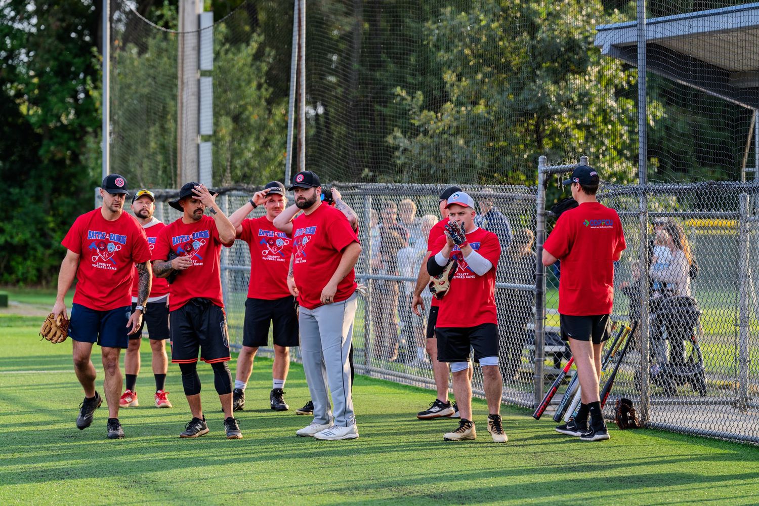 Team of players in red uniforms gathered on baseball field during charity softball game.